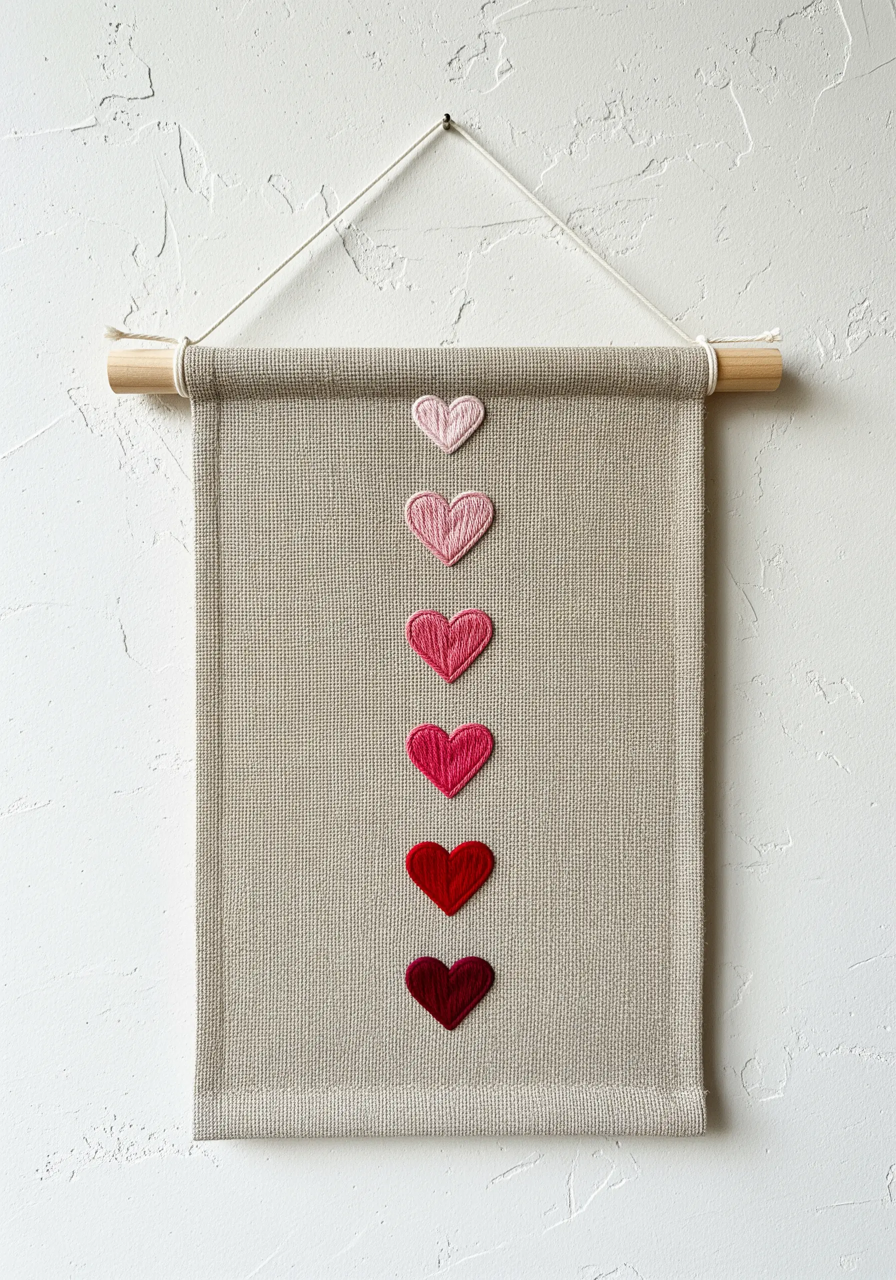 A vertical series of six hearts on a wall hanging, transitioning in color from pink to deep red.