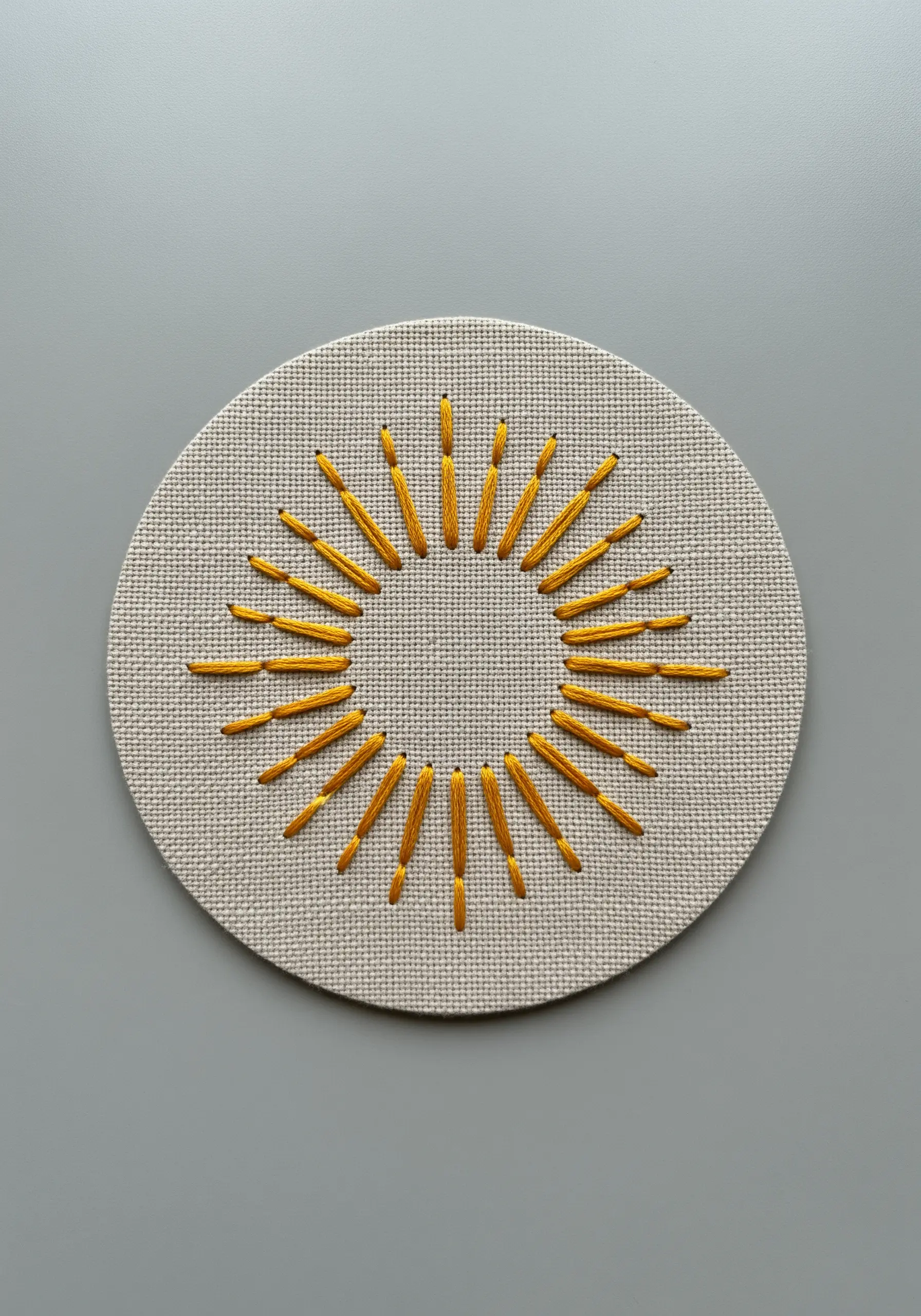 A sun motif with layered straight stitches in yellow on Aida cloth.