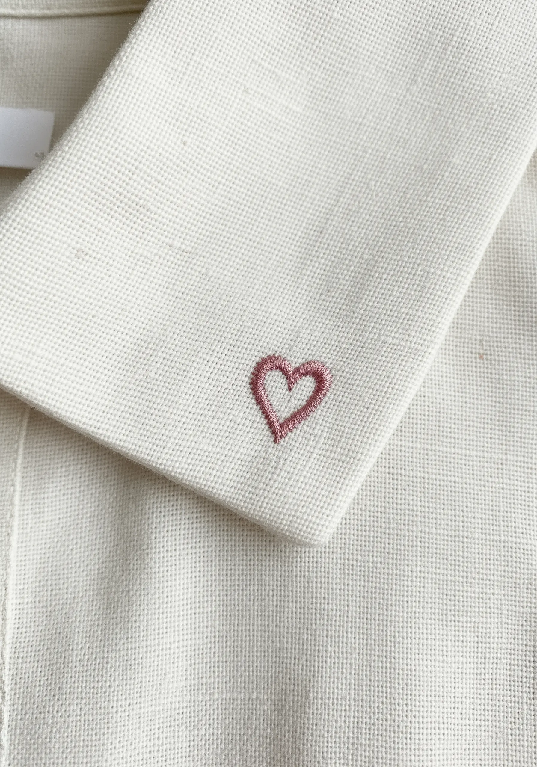 A tiny pink heart embroidered with split stitch on the corner of a white collar.