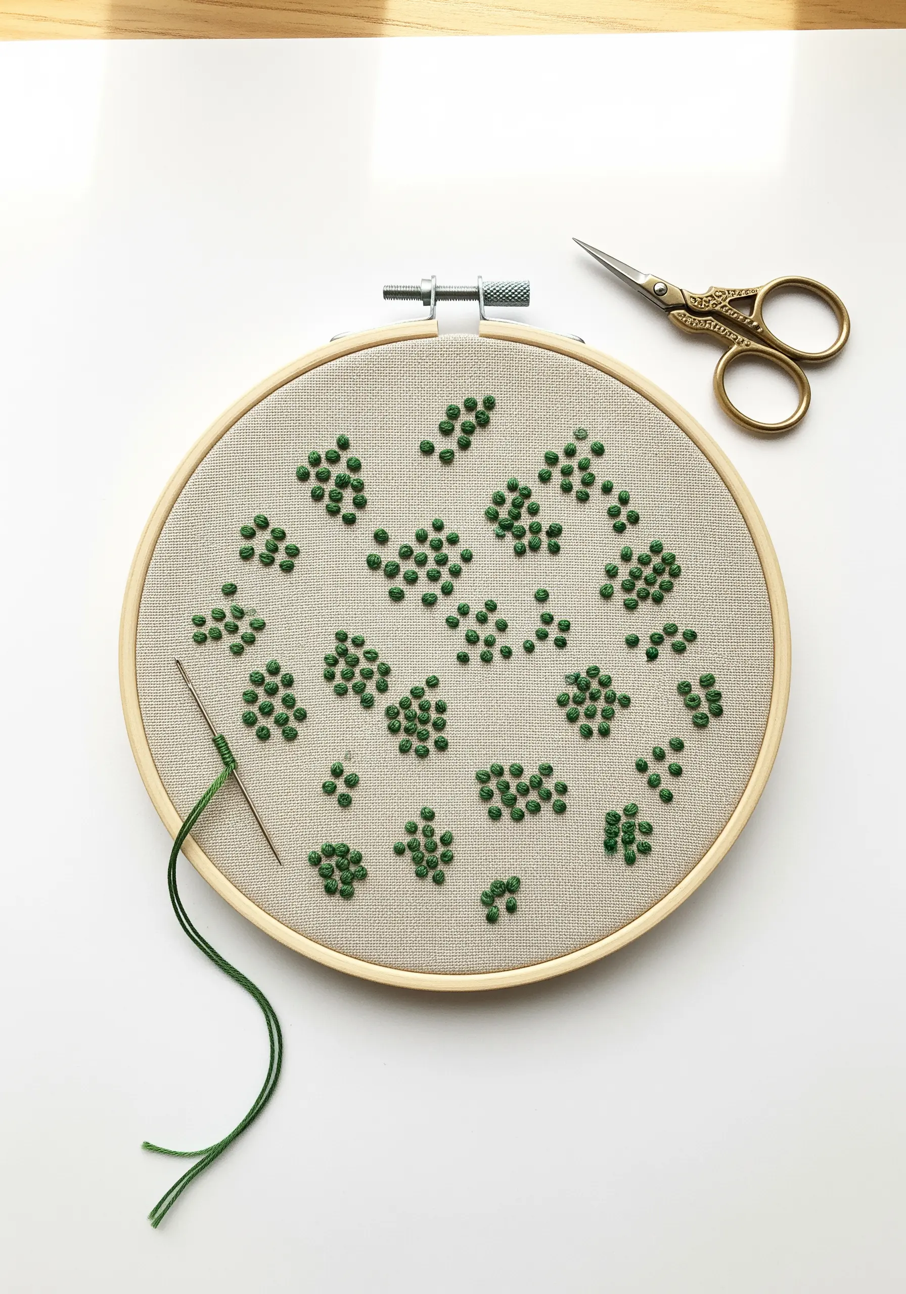 Scattered clusters of green French knots creating an abstract pattern in a hoop.