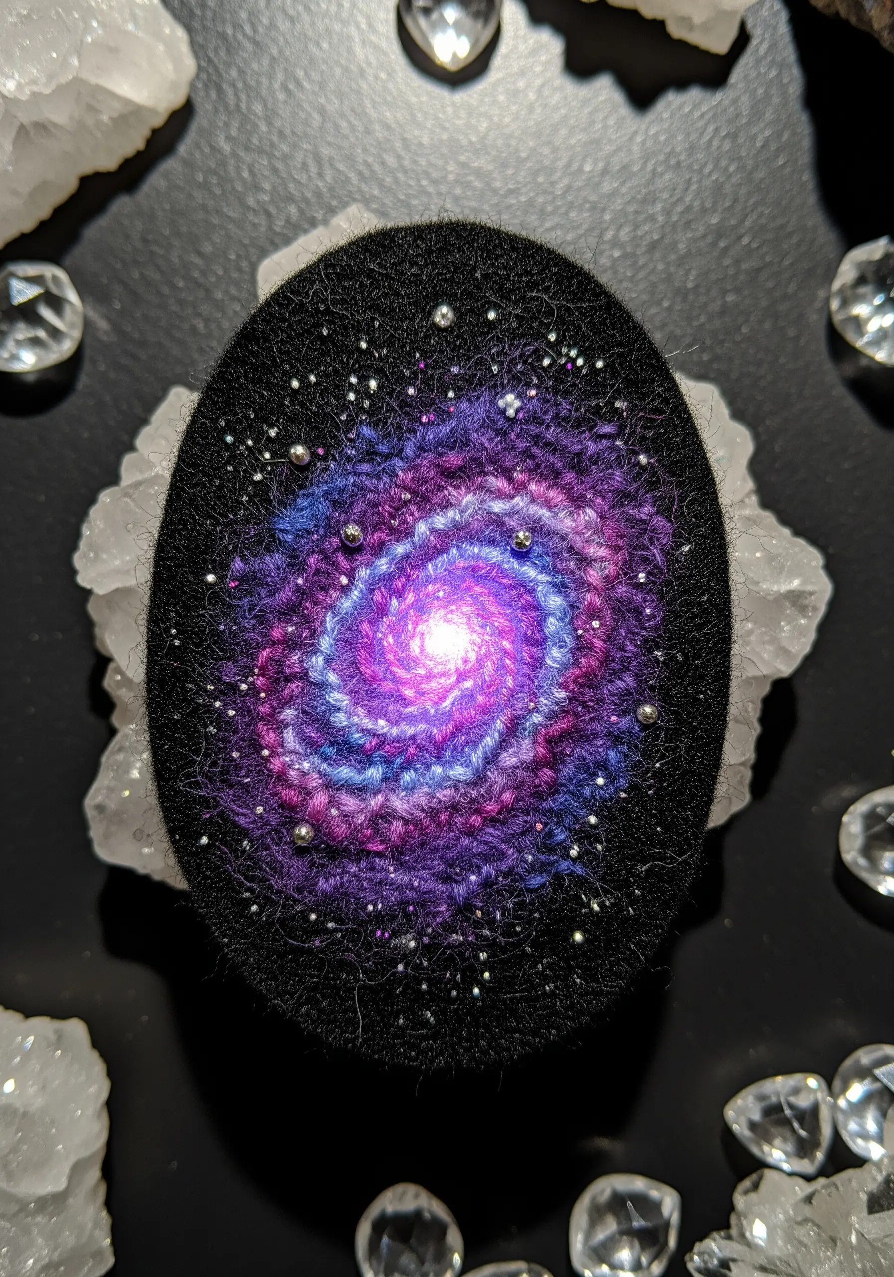 A mixed-media galaxy design on an oval felt patch, combining needle felting with embroidered stars and beads.