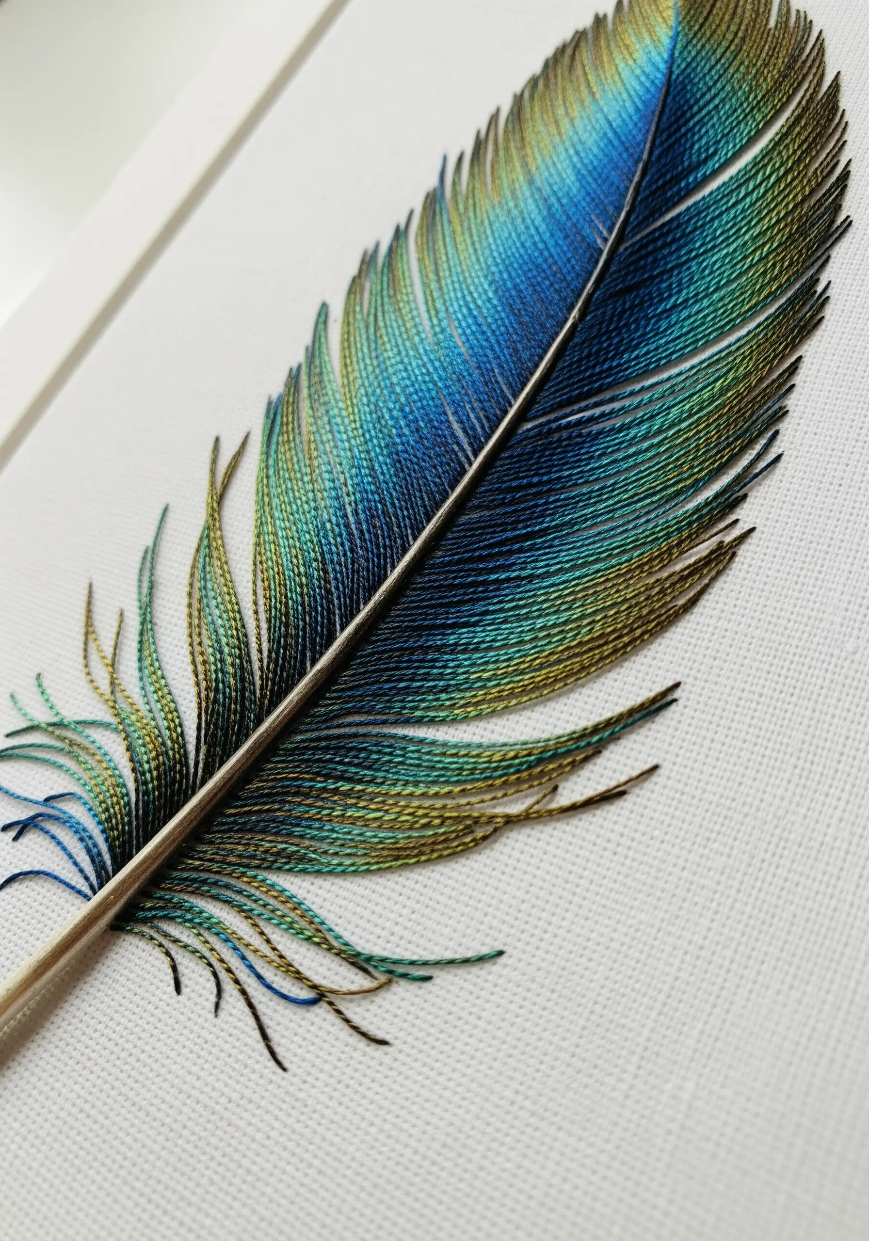 A hyper-realistic peacock feather embroidered with seamlessly blended blue, green, and gold threads.
