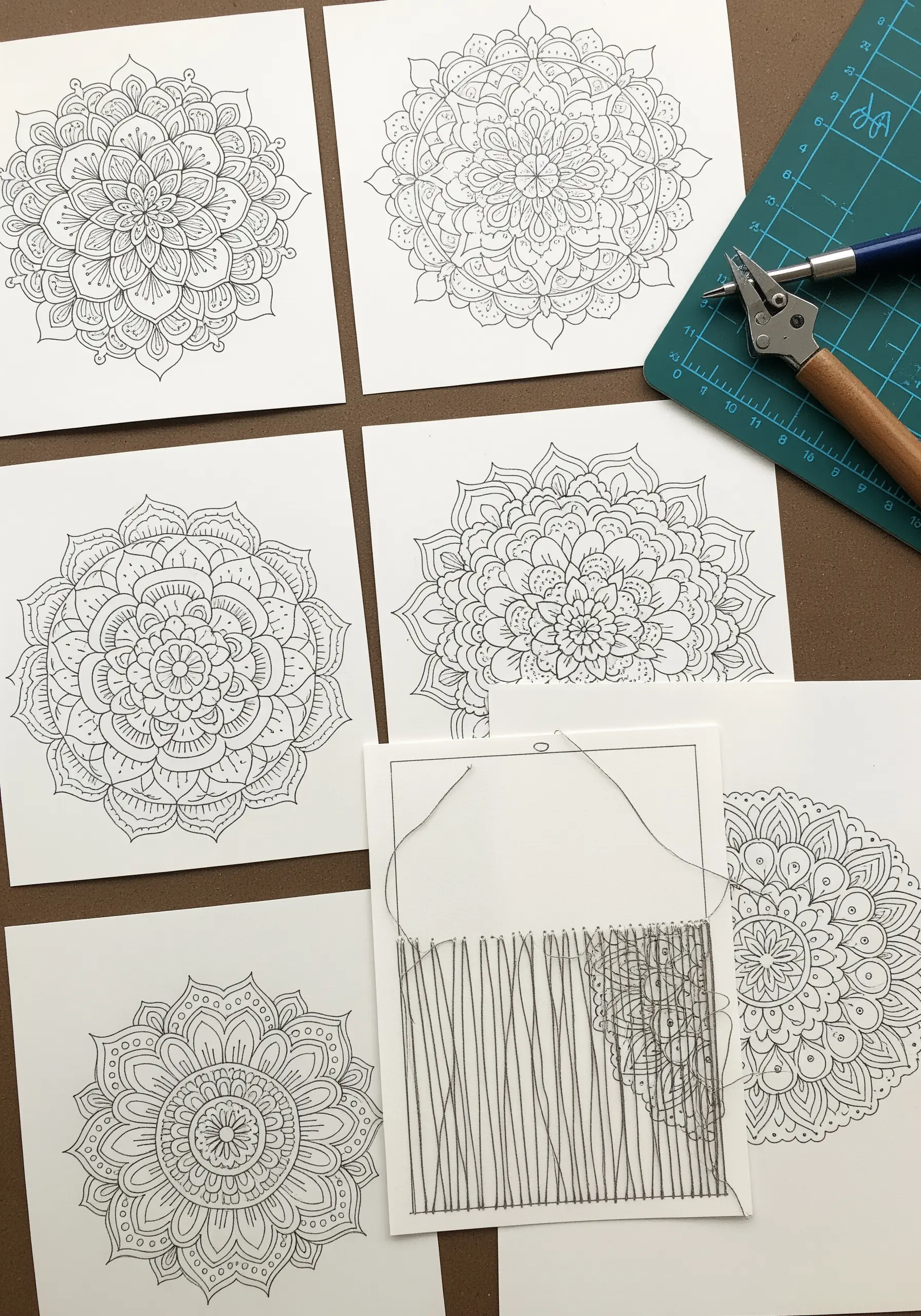 A paper embroidery project in progress, showing a needle pulling thread through pre-pierced mandala patterns.