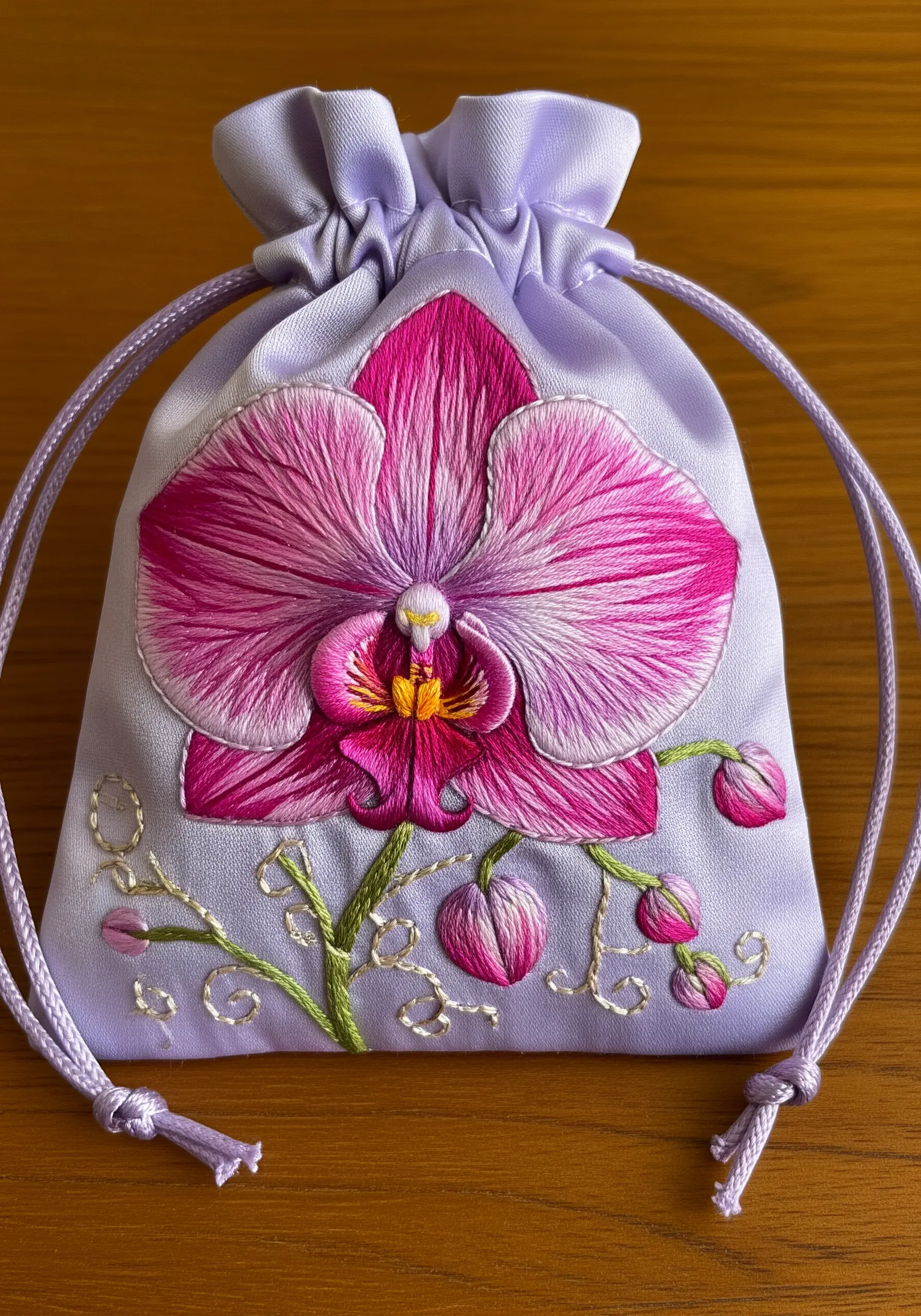 A pink and magenta orchid with gradient petals stitched on a light purple satin pouch.