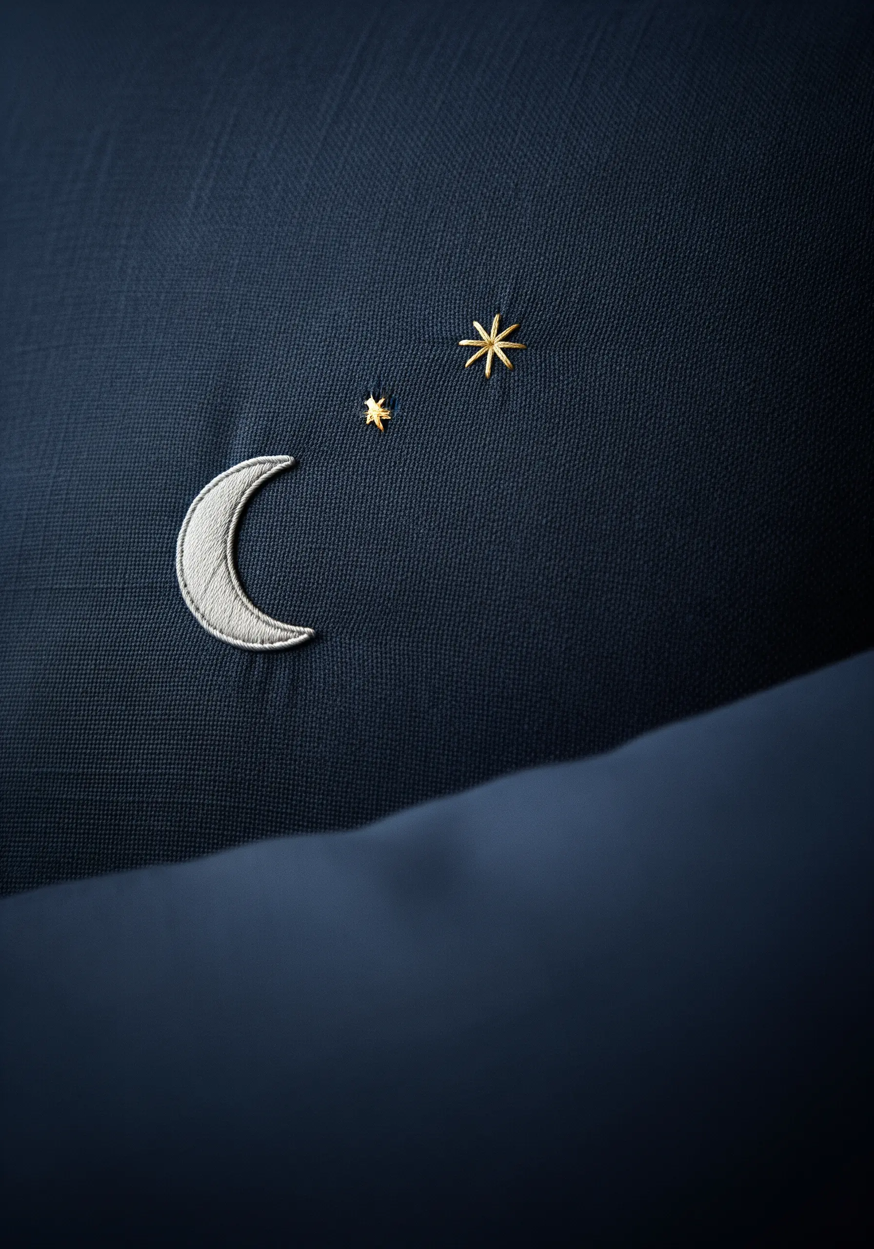 A silver crescent moon and gold stars embroidered on a dark navy blue pillow.