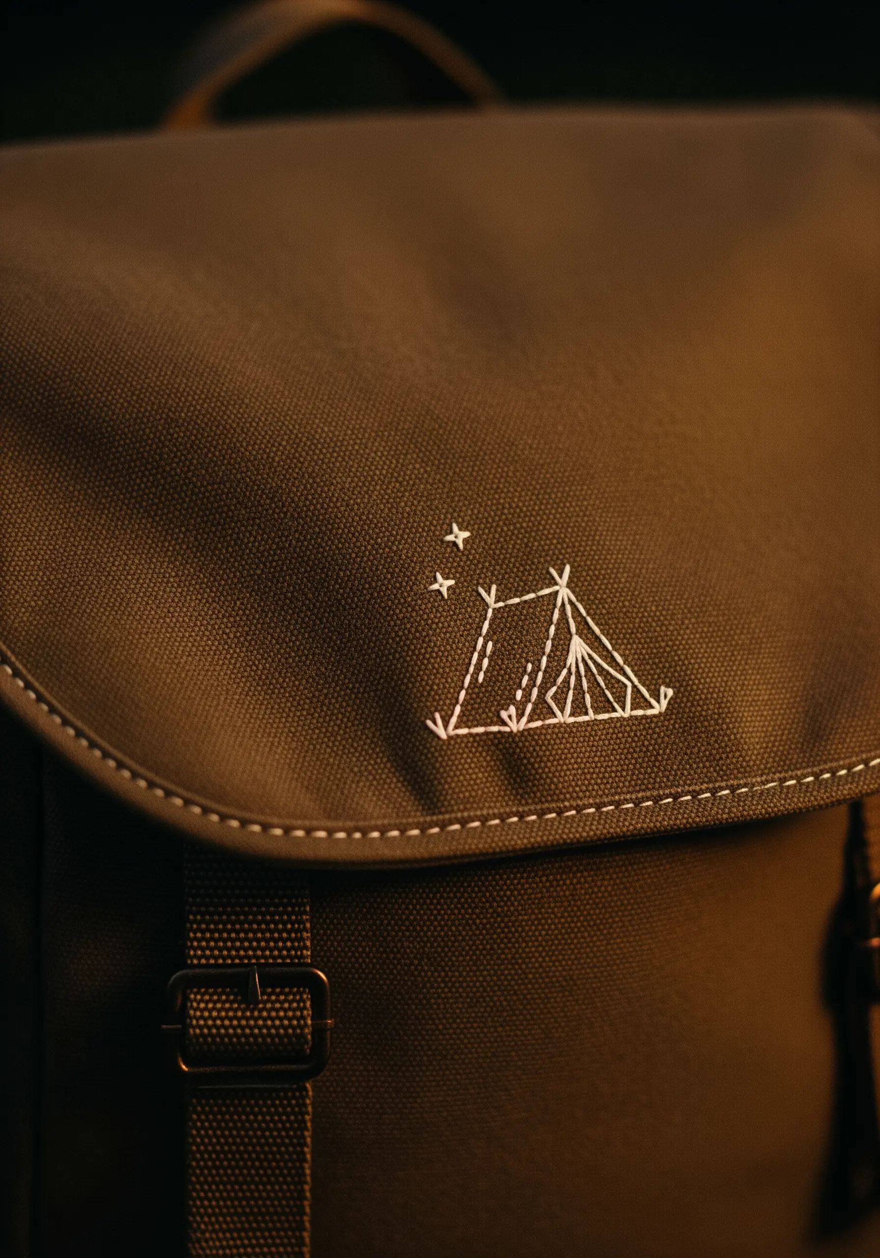 A minimalist white outline of a tent and three stars on the flap of a dark canvas backpack.