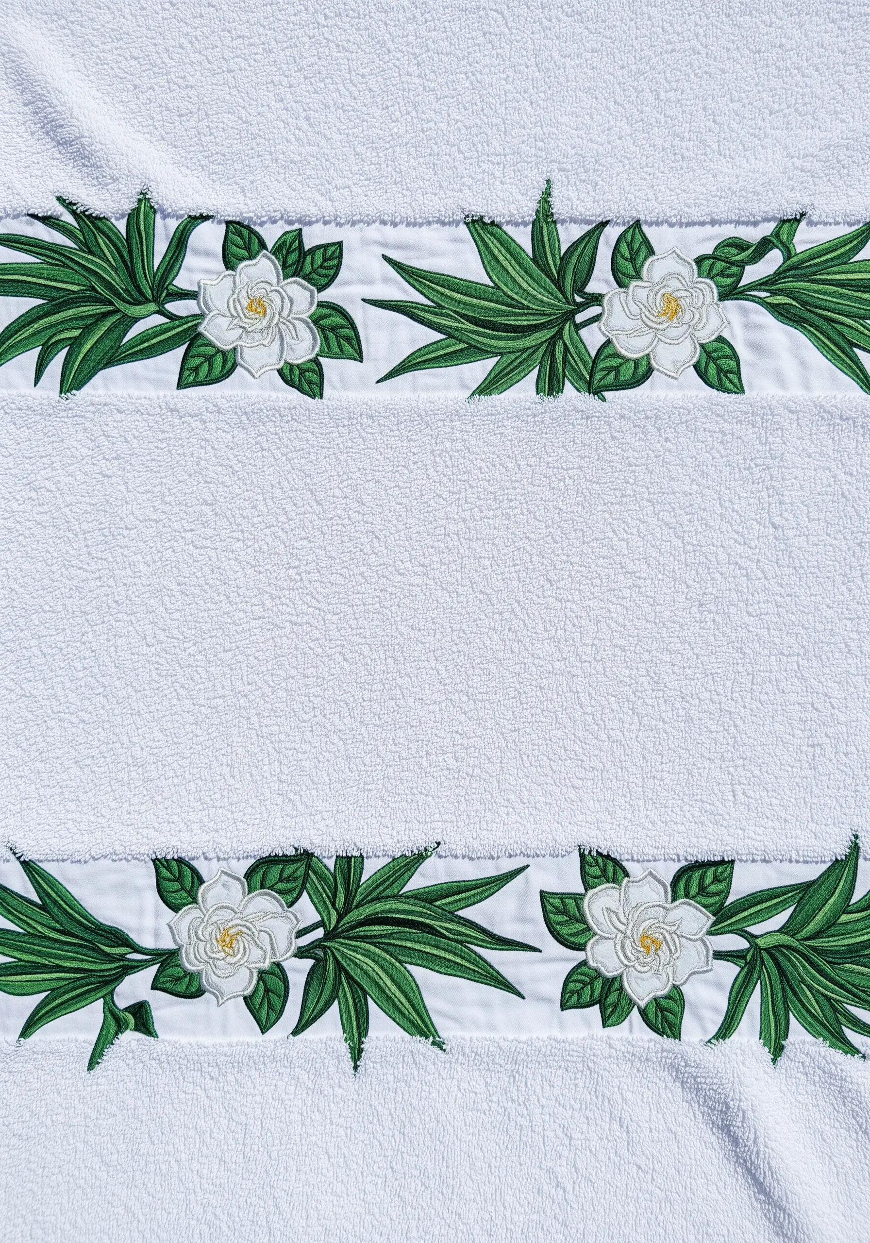 A white terry cloth towel with an elegant embroidered border of white gardenias and green leaves.