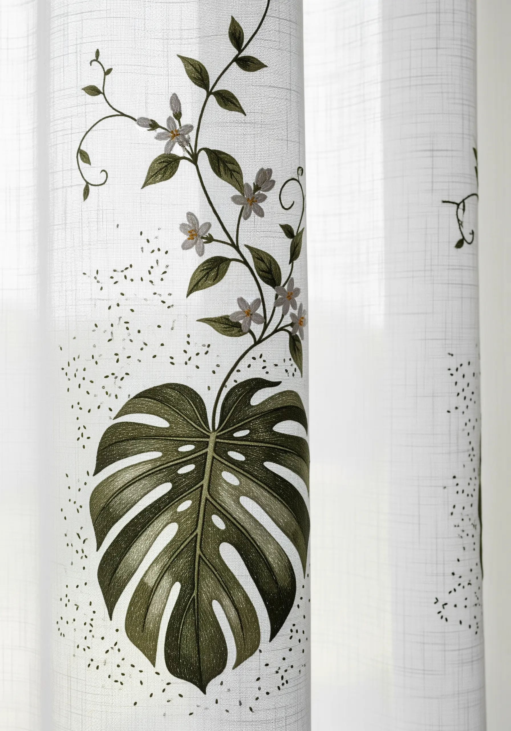 A delicate vine and a large monstera leaf embroidered on a sheer, light-filtering white curtain.