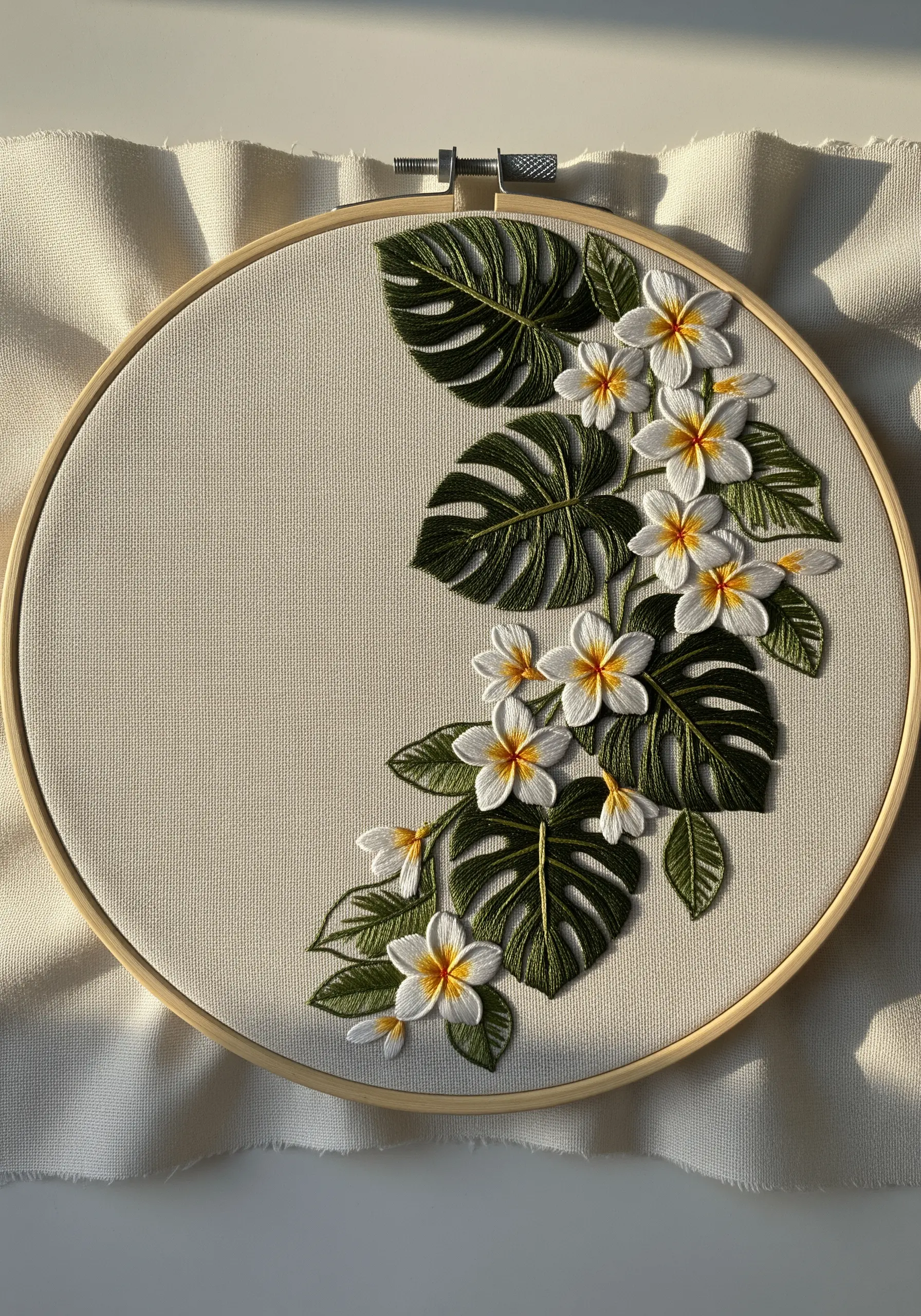 3D plumeria flowers and monstera leaves arranged in a crescent shape within an embroidery hoop.