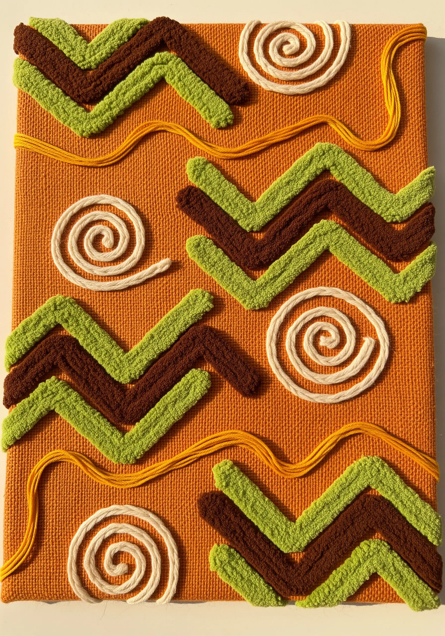 Textured embroidery with raised green and brown zigzags and flat cream spirals on orange fabric.