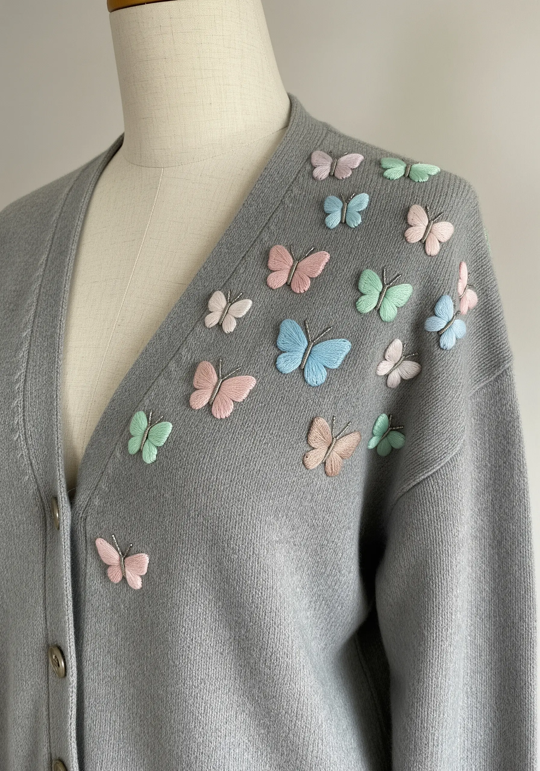 Three-dimensional pastel butterflies embroidered onto the shoulder of a grey cardigan.
