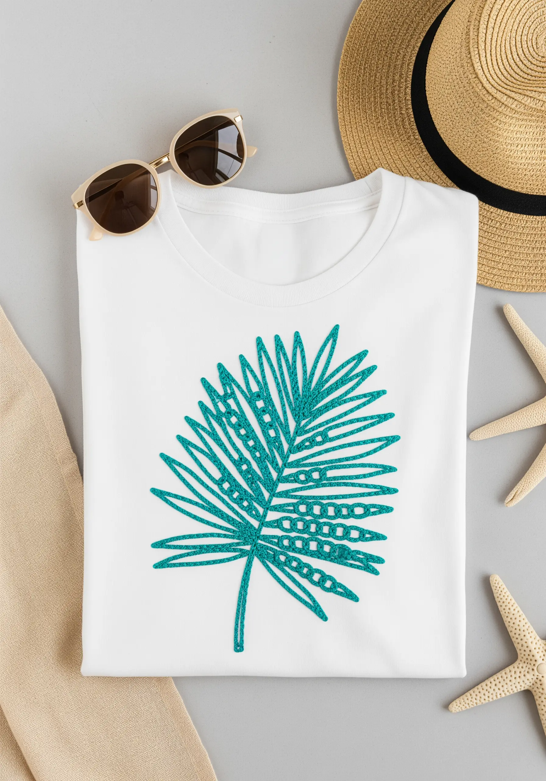 A large teal palm frond with decorative fill stitches on a white t-shirt.