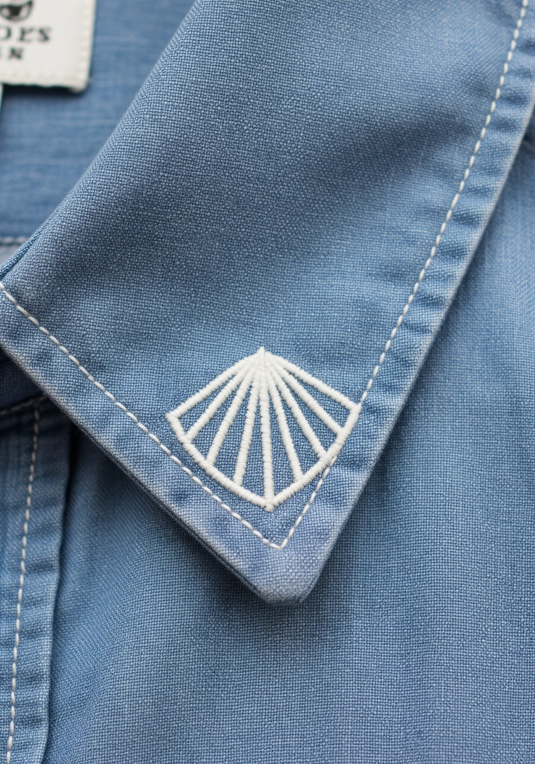 A white geometric fan motif embroidered on the corner of a blue denim collar.