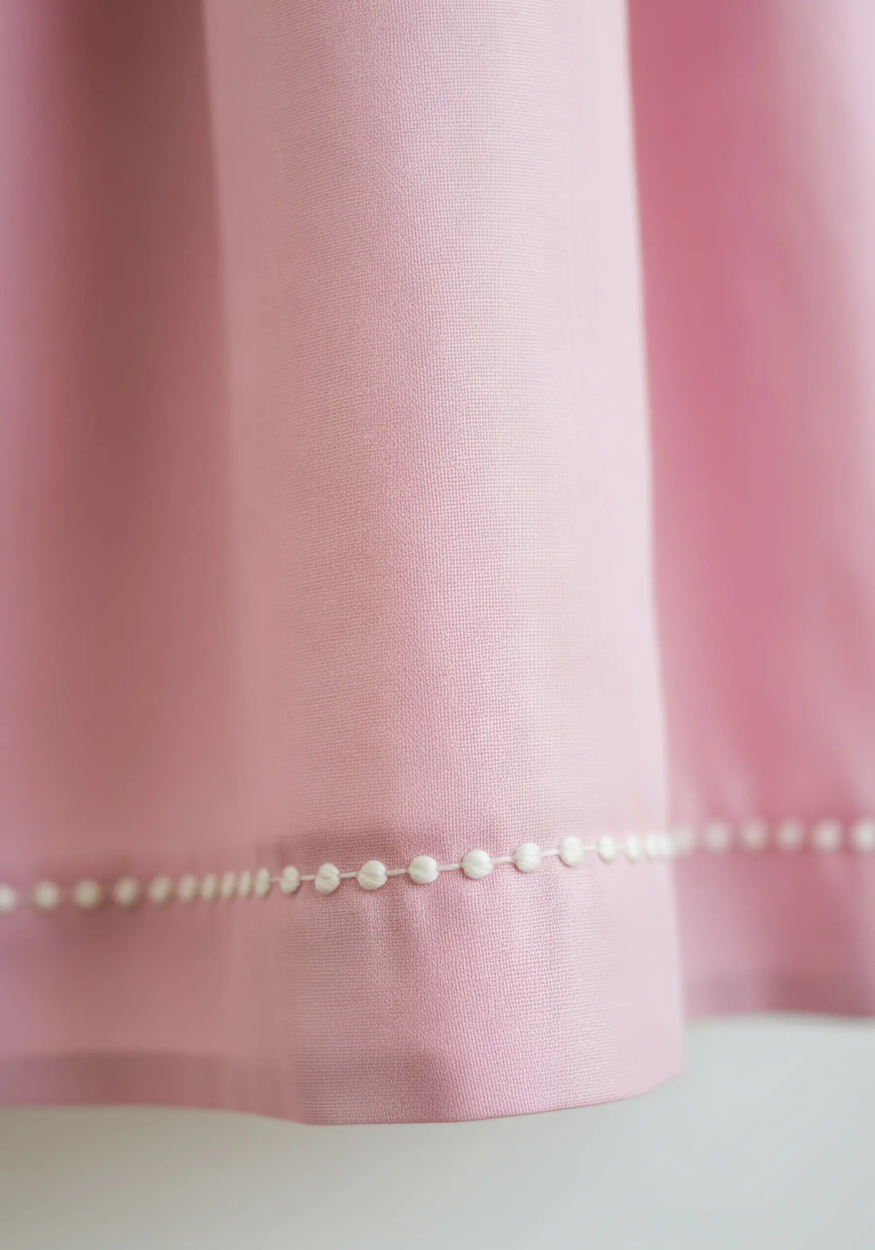 A delicate beaded border stitch in white thread on the hem of pink fabric.