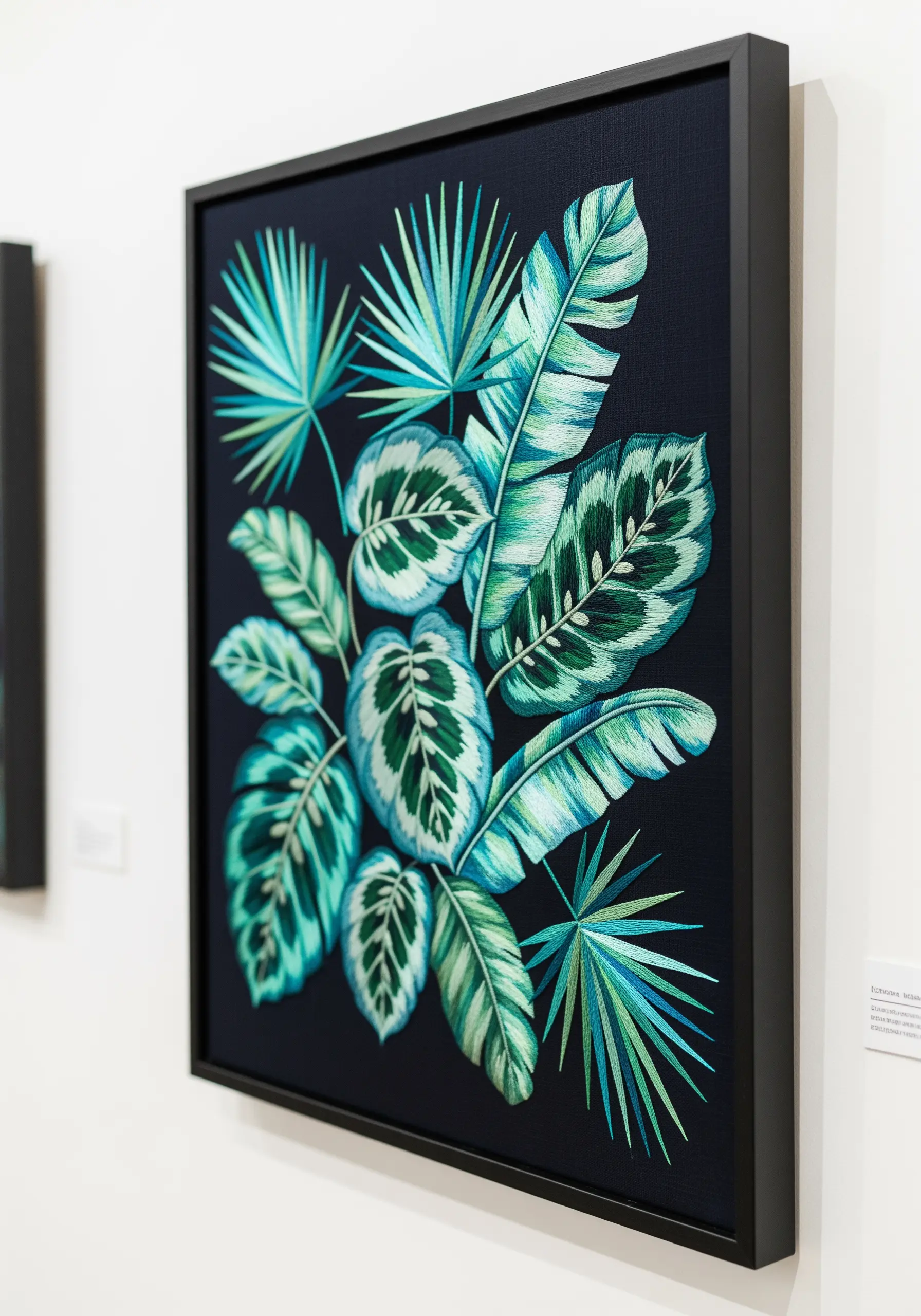 Framed embroidery of vibrant tropical leaves in shades of teal and green on a black canvas.