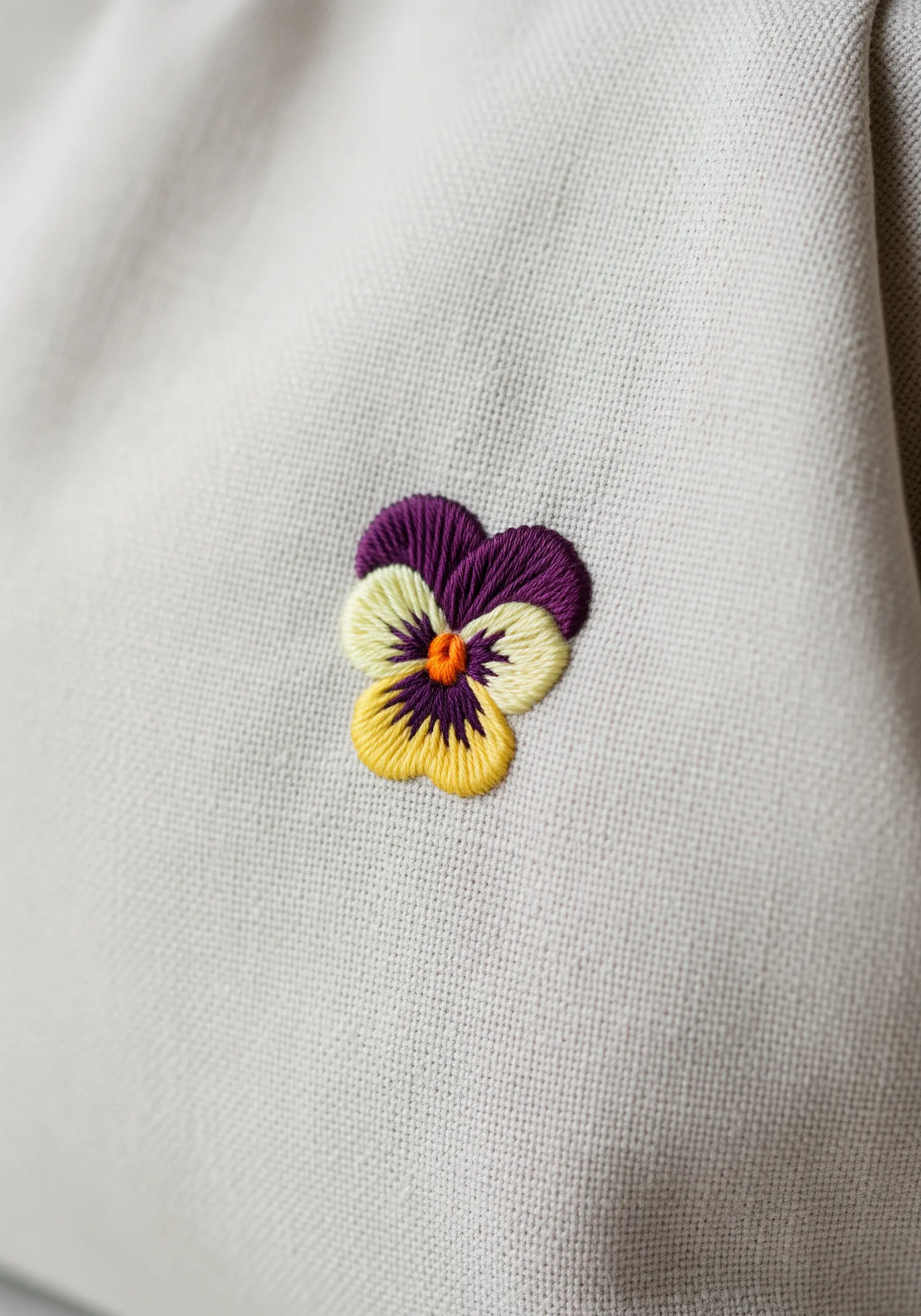 A small, detailed embroidered pansy with purple, yellow, and orange petals.