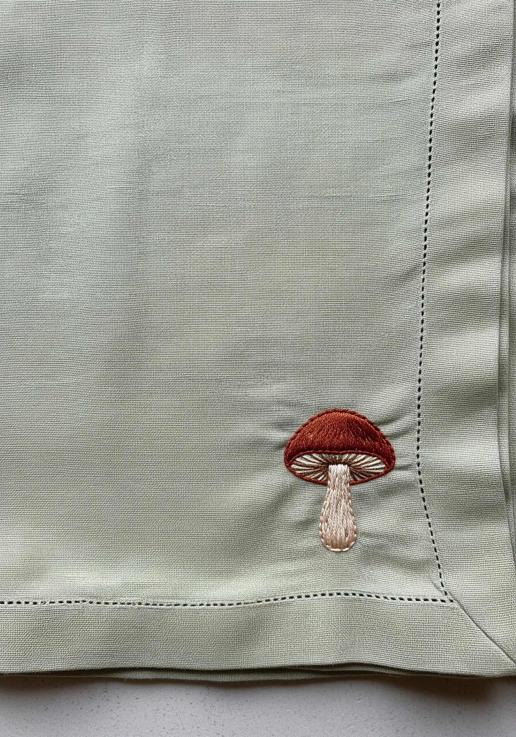 A small embroidered mushroom with a thread-painted cap on a green linen napkin.
