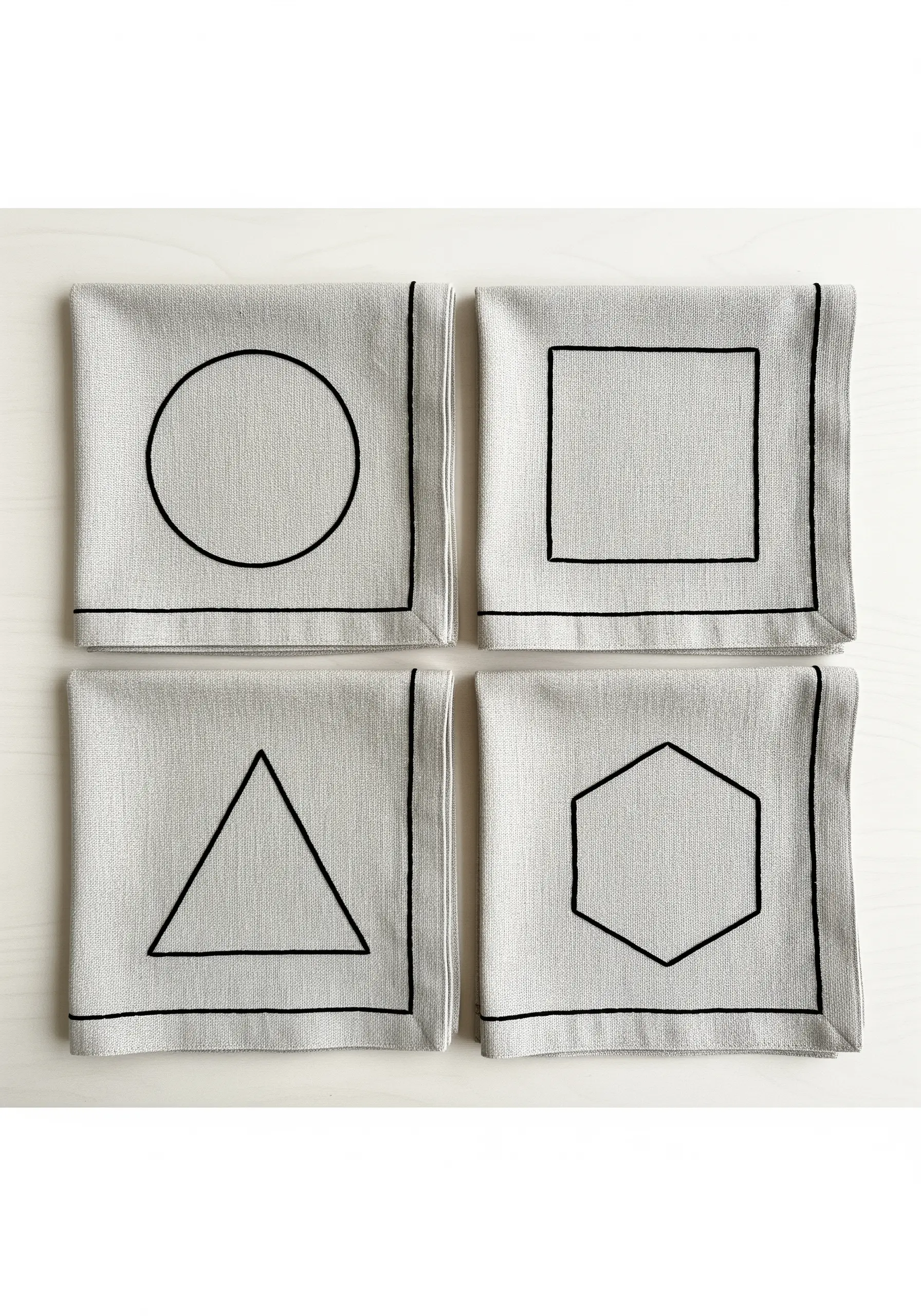 Four linen coasters, each with a different black geometric shape outlined in thread.