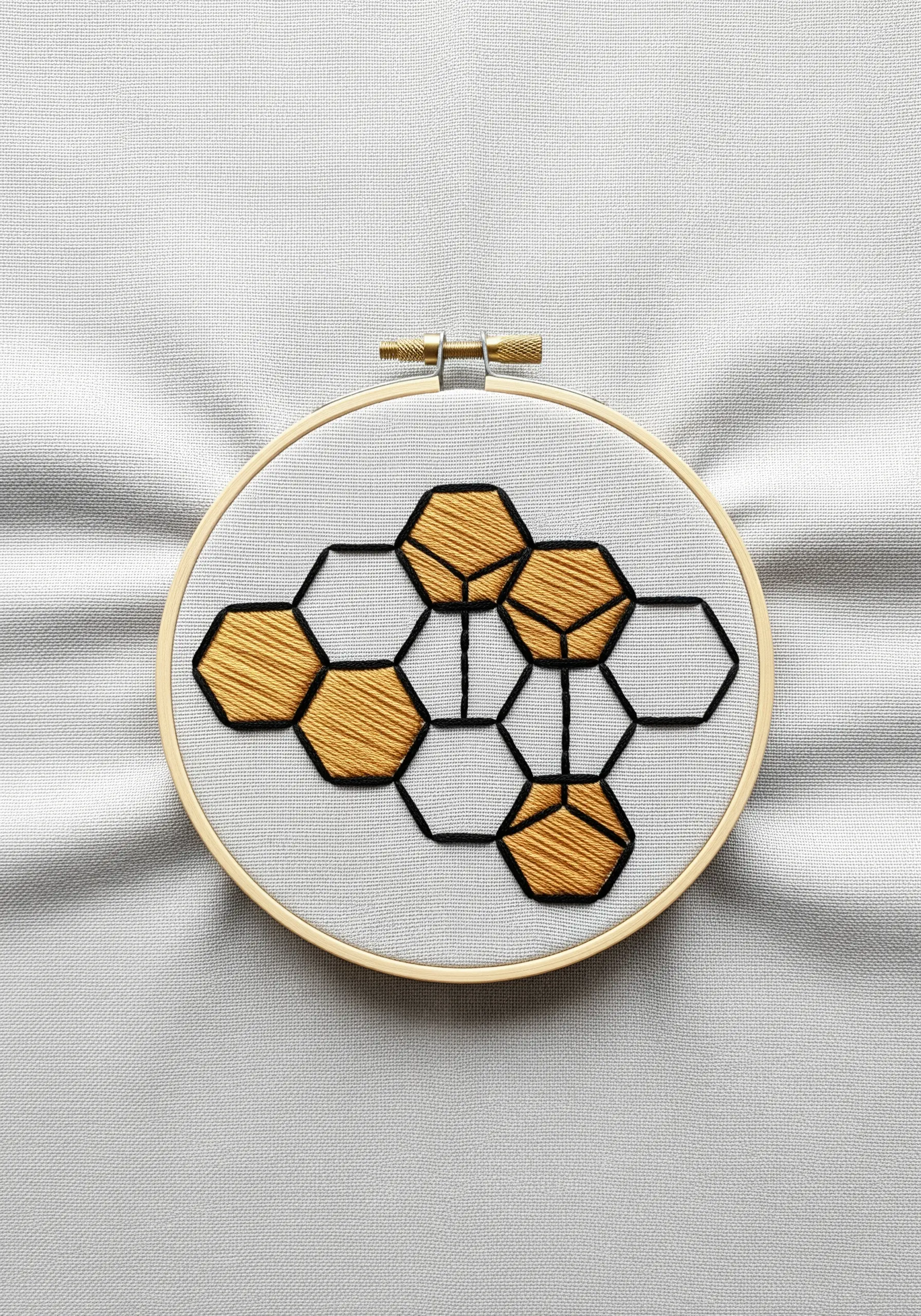 A geometric honeycomb pattern with 3D-effect satin stitches in gold and black.