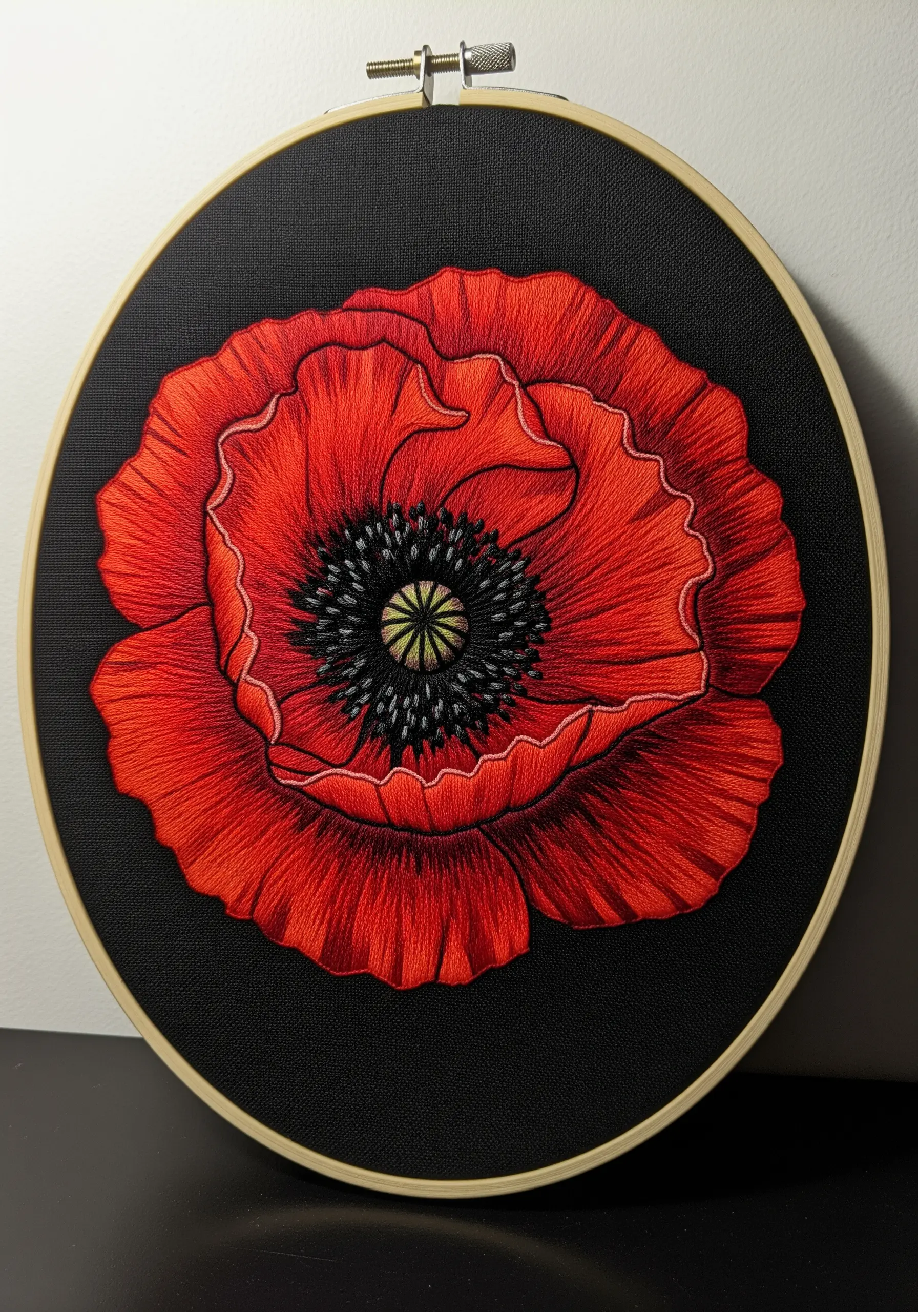 A vibrant red poppy with a textured black center, stitched on dark fabric.