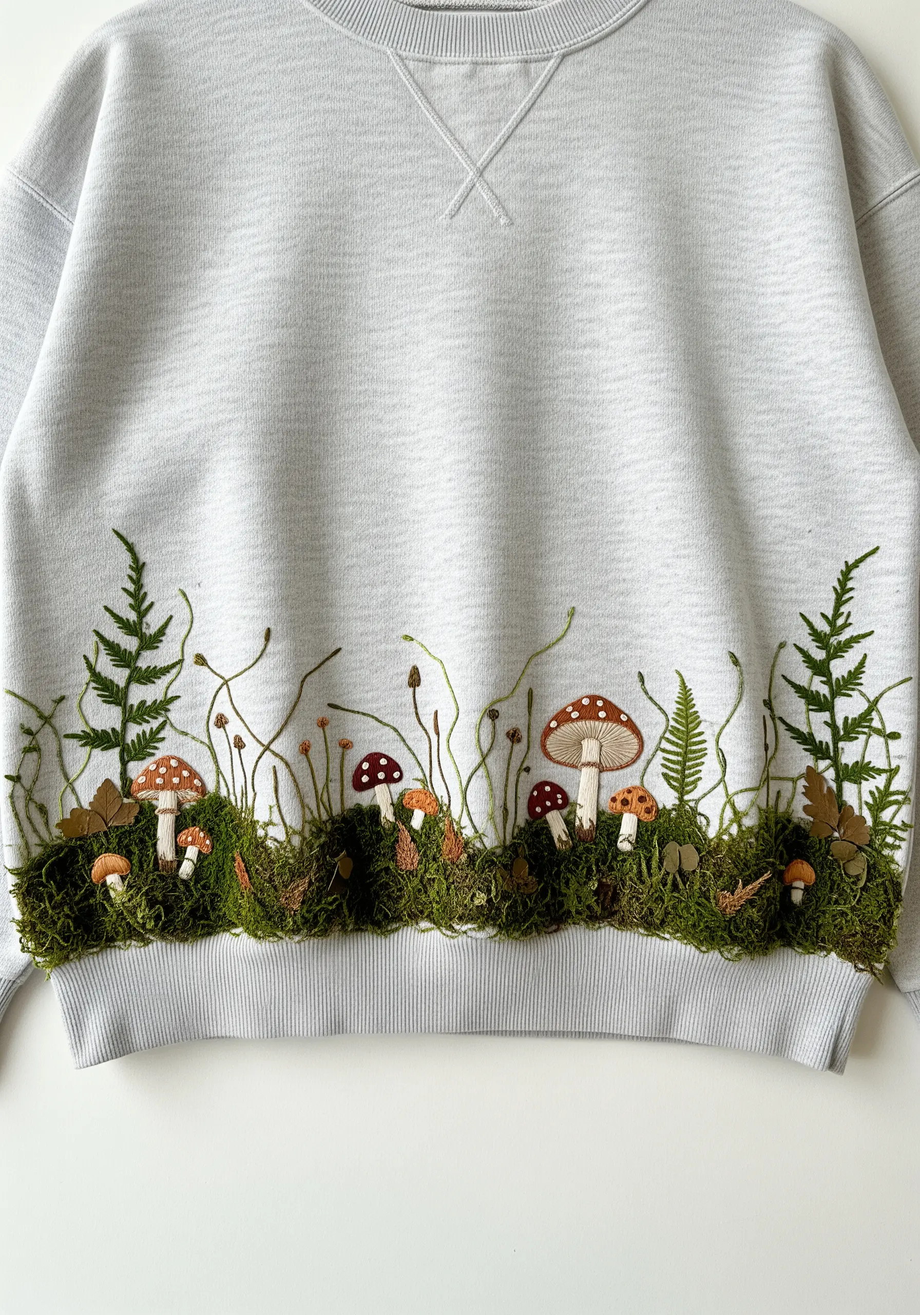 The bottom hem of a sweatshirt is decorated with real moss, embroidered mushrooms, and ferns.