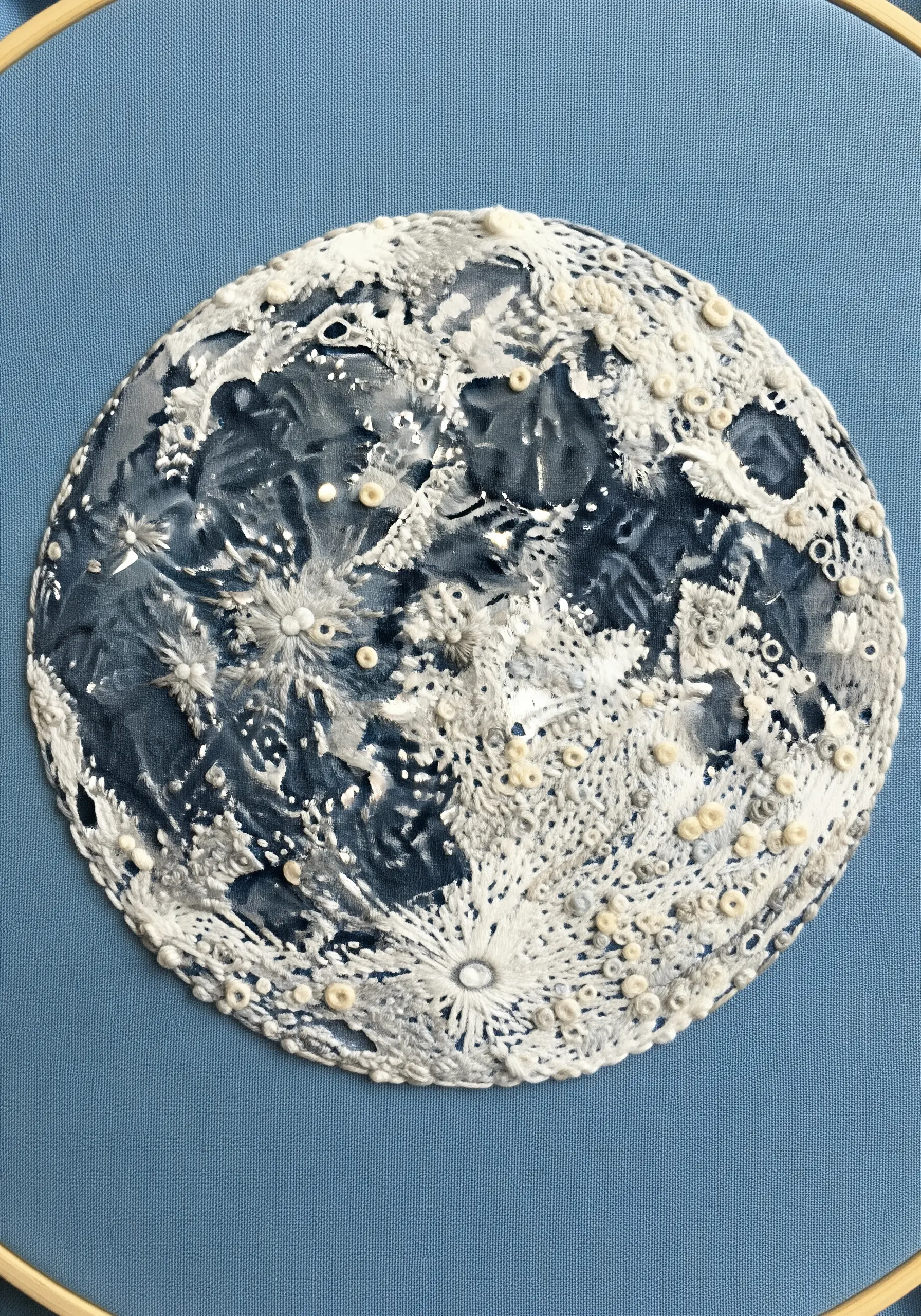 A highly detailed, textured full moon embroidery using French knots and layered stitches.