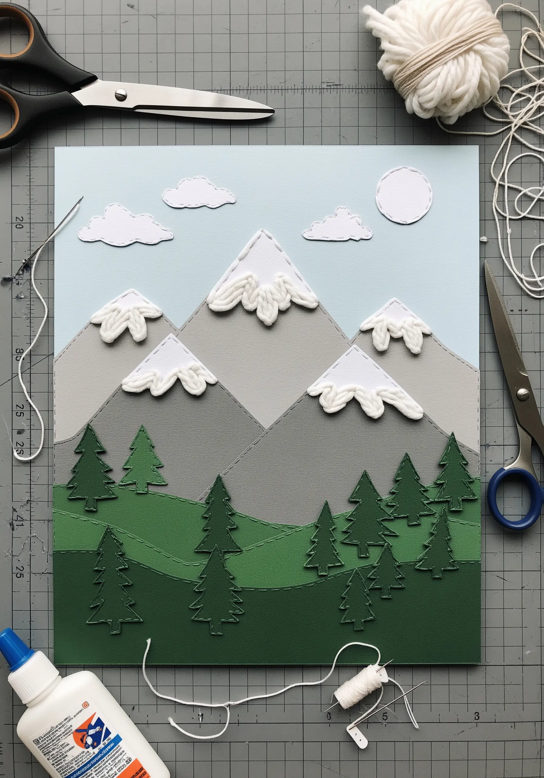 A layered paper art piece of a mountain scene with stitched details and yarn snowcaps.