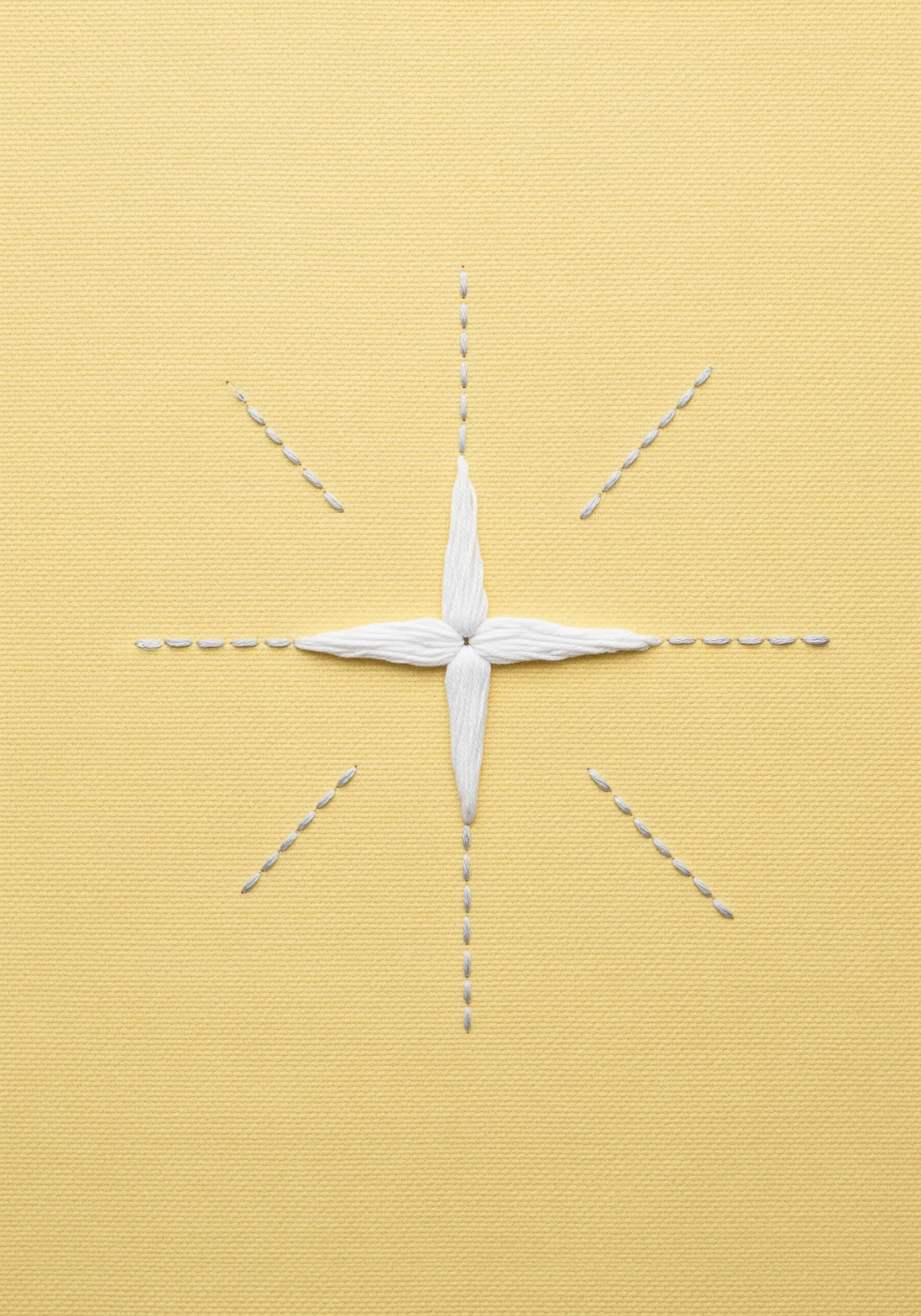 A central star made of layered satin stitches with radiating lines of seed stitches on yellow fabric.