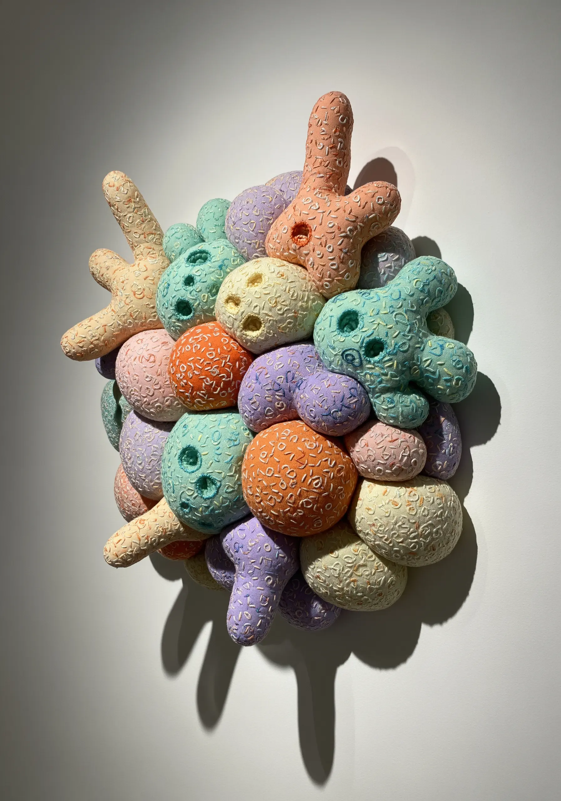 A 3D cluster of pastel-colored, stuffed fabric shapes covered in tiny embroidered patterns.