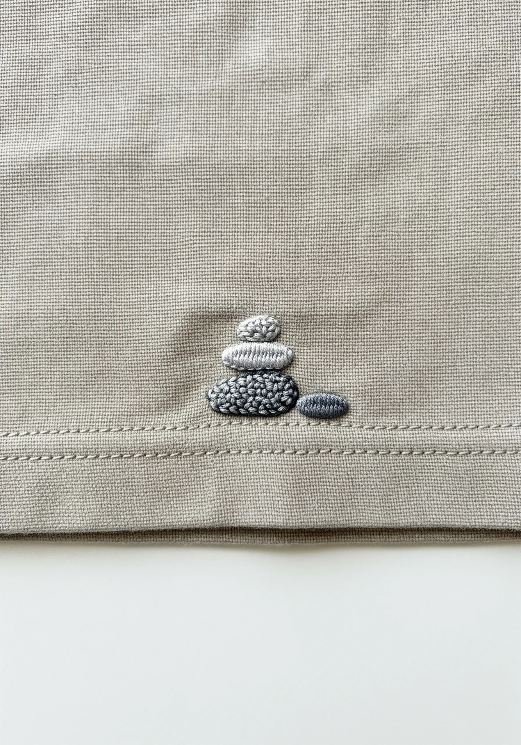 A small stack of pebbles embroidered on a beige shirt, using French knots of varying textures.