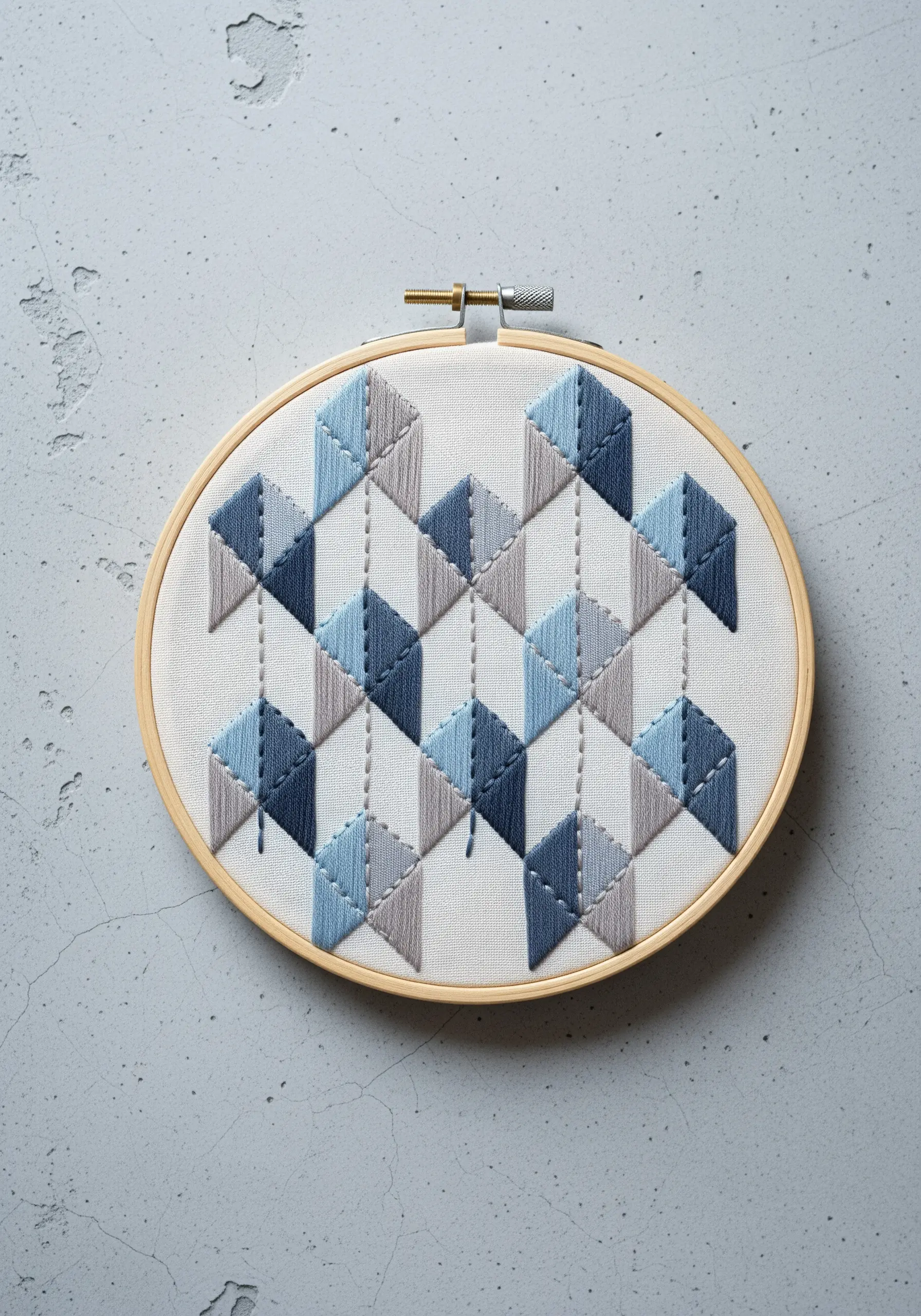 A geometric pattern of 3D cubes in shades of blue and gray satin stitch.