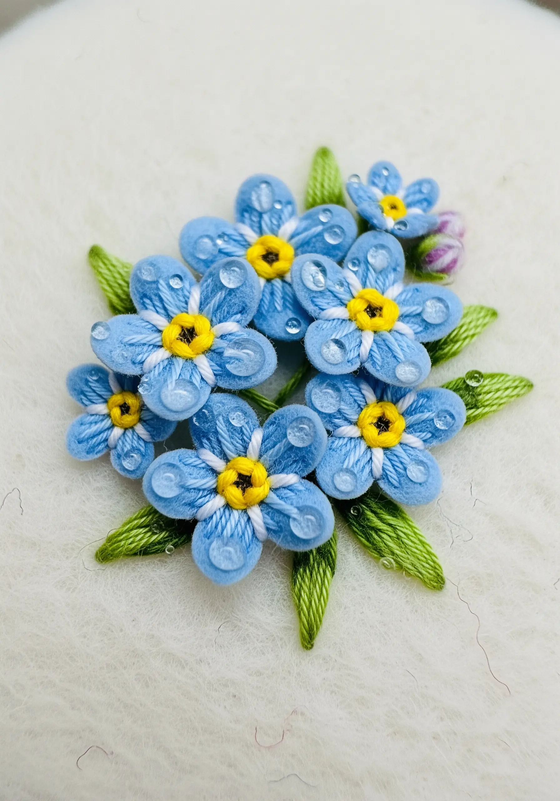 Small blue forget-me-not flowers with a soft, fuzzy texture stitched on white felt.