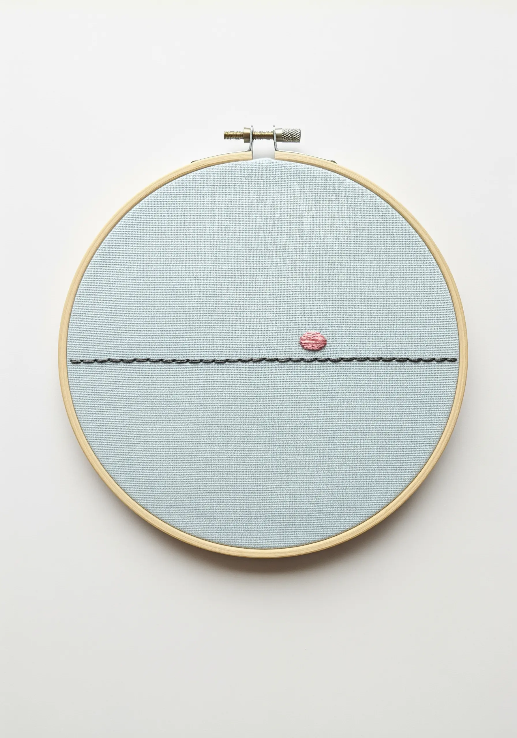 A minimalist sunset with a black horizon line and a small pink satin-stitched sun.