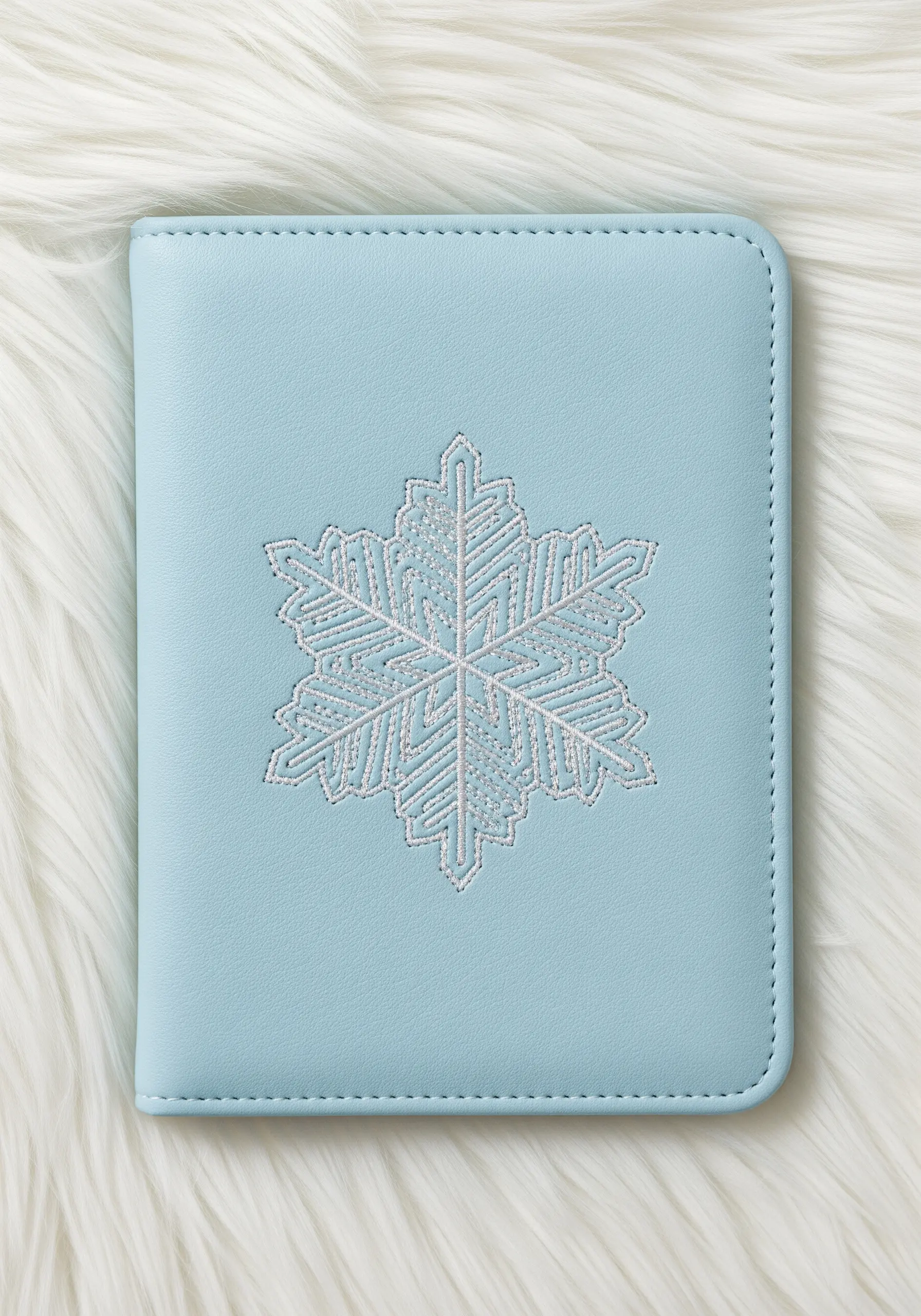 An intricate white and silver snowflake embroidered on a light blue passport cover.