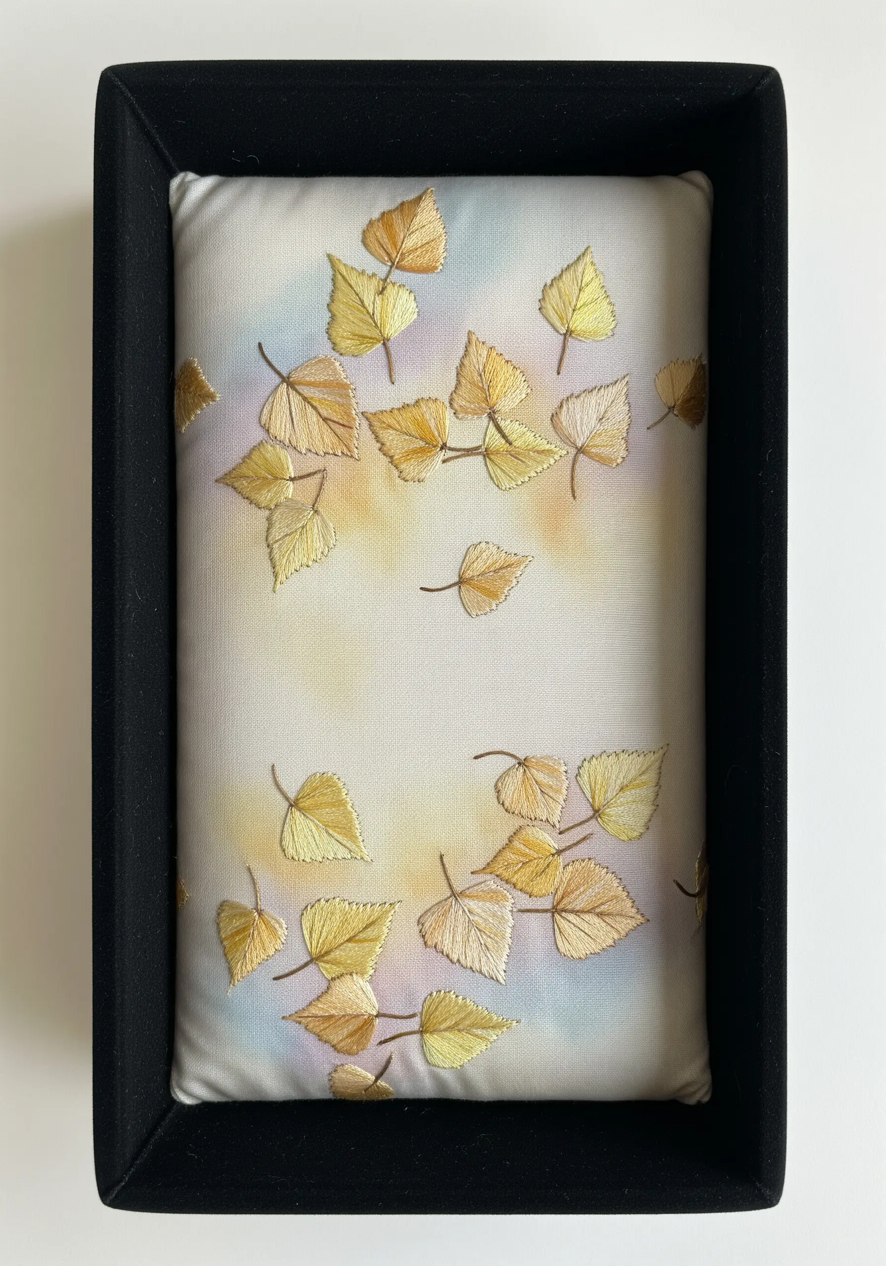 Framed embroidery of golden birch leaves appearing to fall against a soft painted watercolor sky.