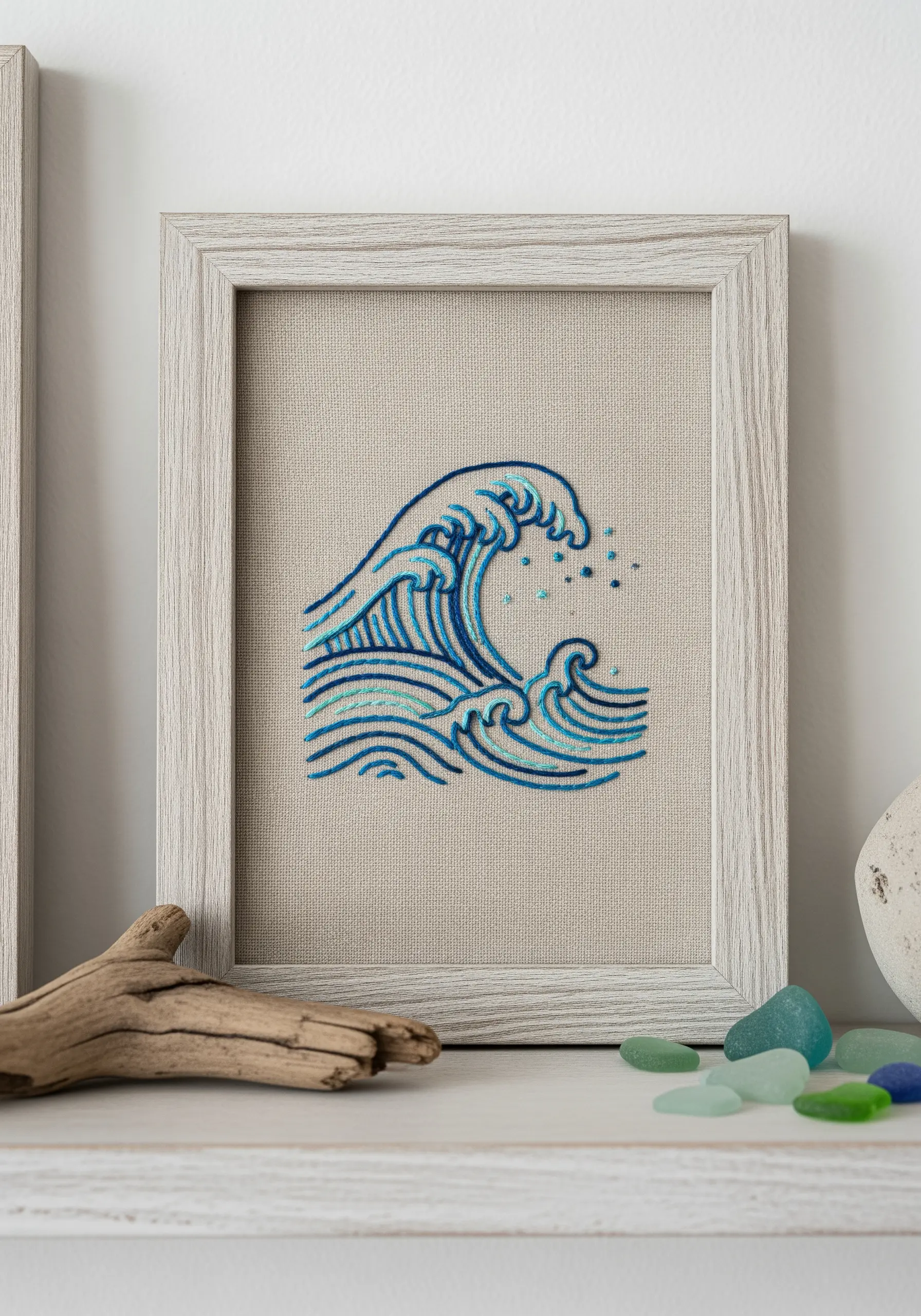 Framed embroidery of a stylized blue ocean wave on linen fabric.