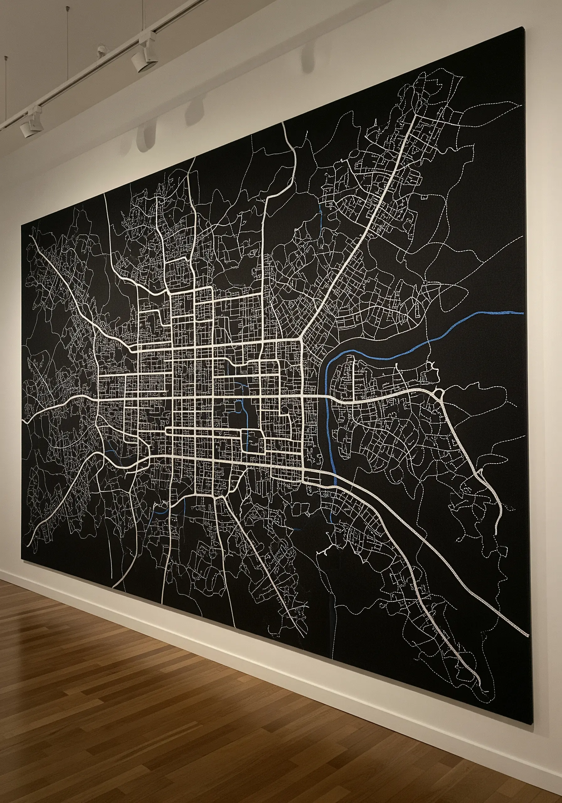 A large black canvas with an intricate city map stitched in white and blue thread.