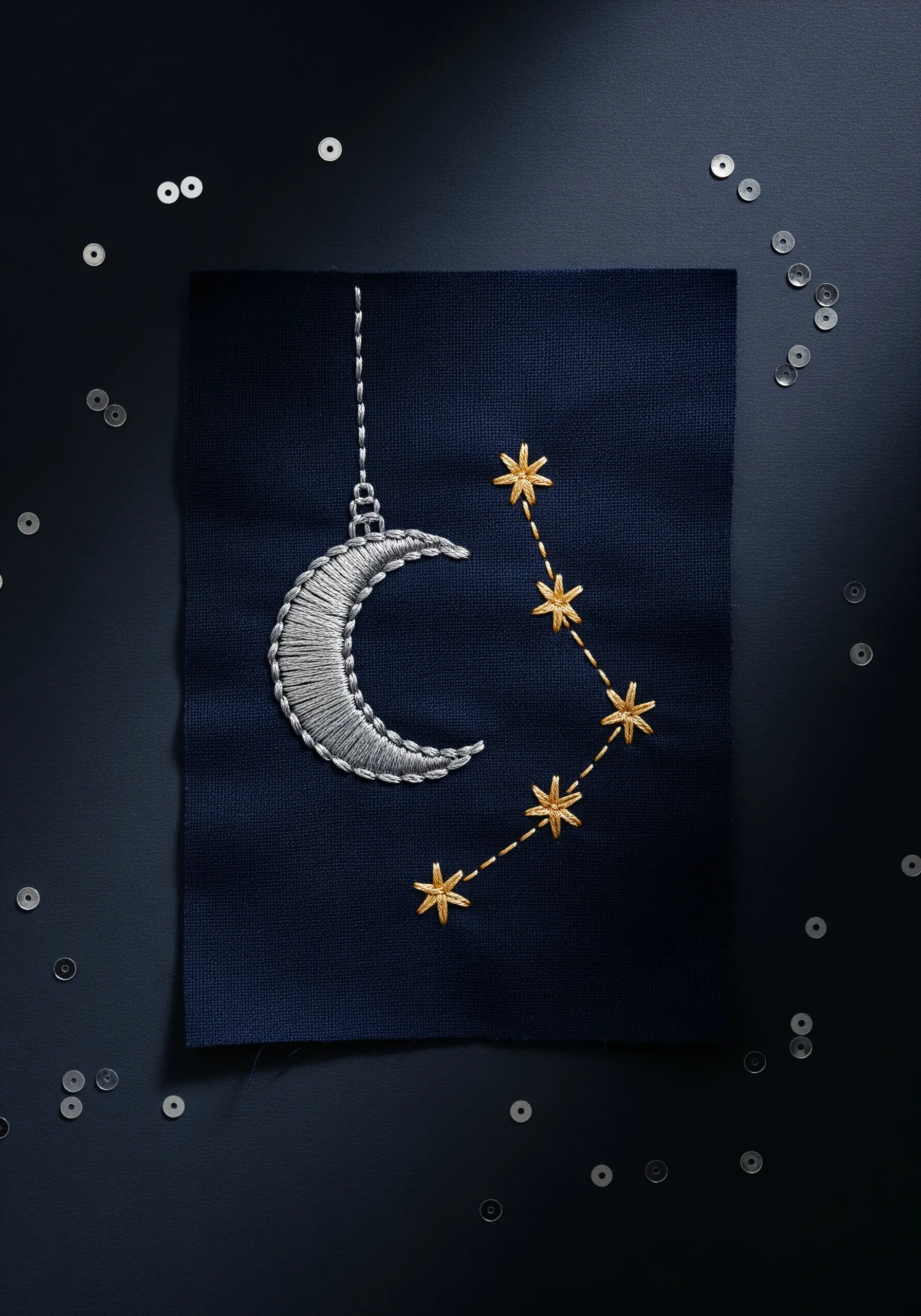 An embroidered silver crescent moon and a gold star constellation on dark navy fabric.