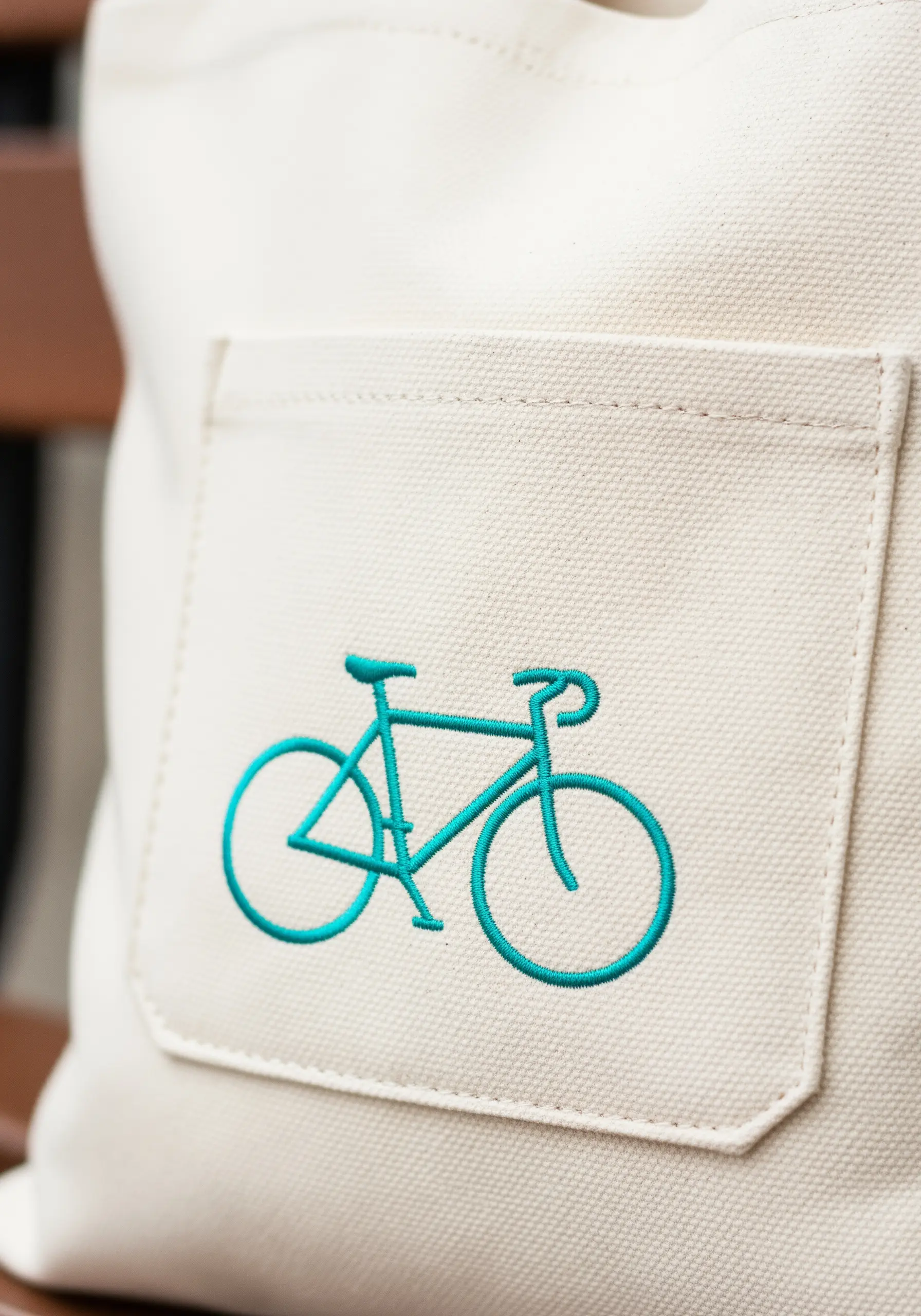 A bright turquoise bicycle embroidered on the pocket of a canvas tote bag.
