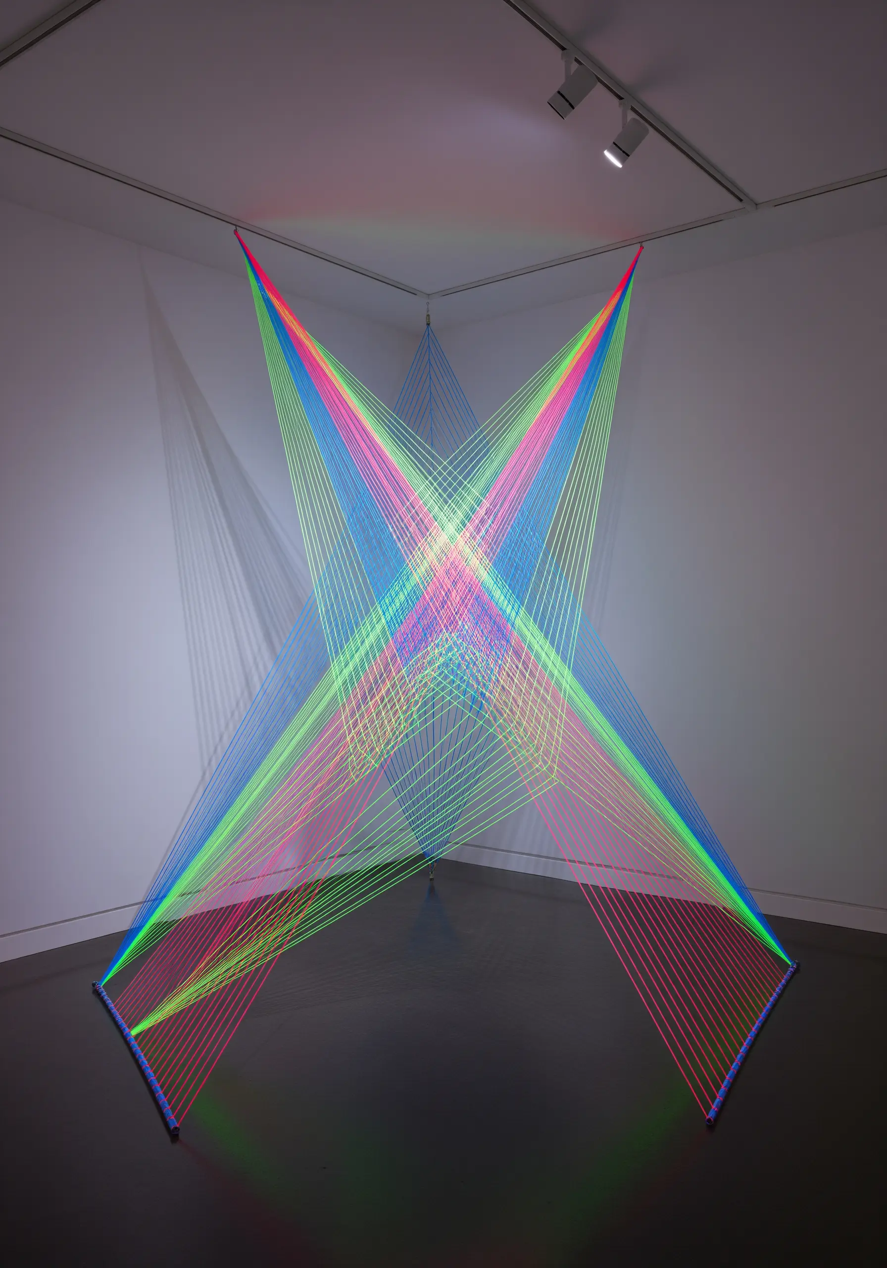 Corner installation of intersecting neon string art in vibrant colors.