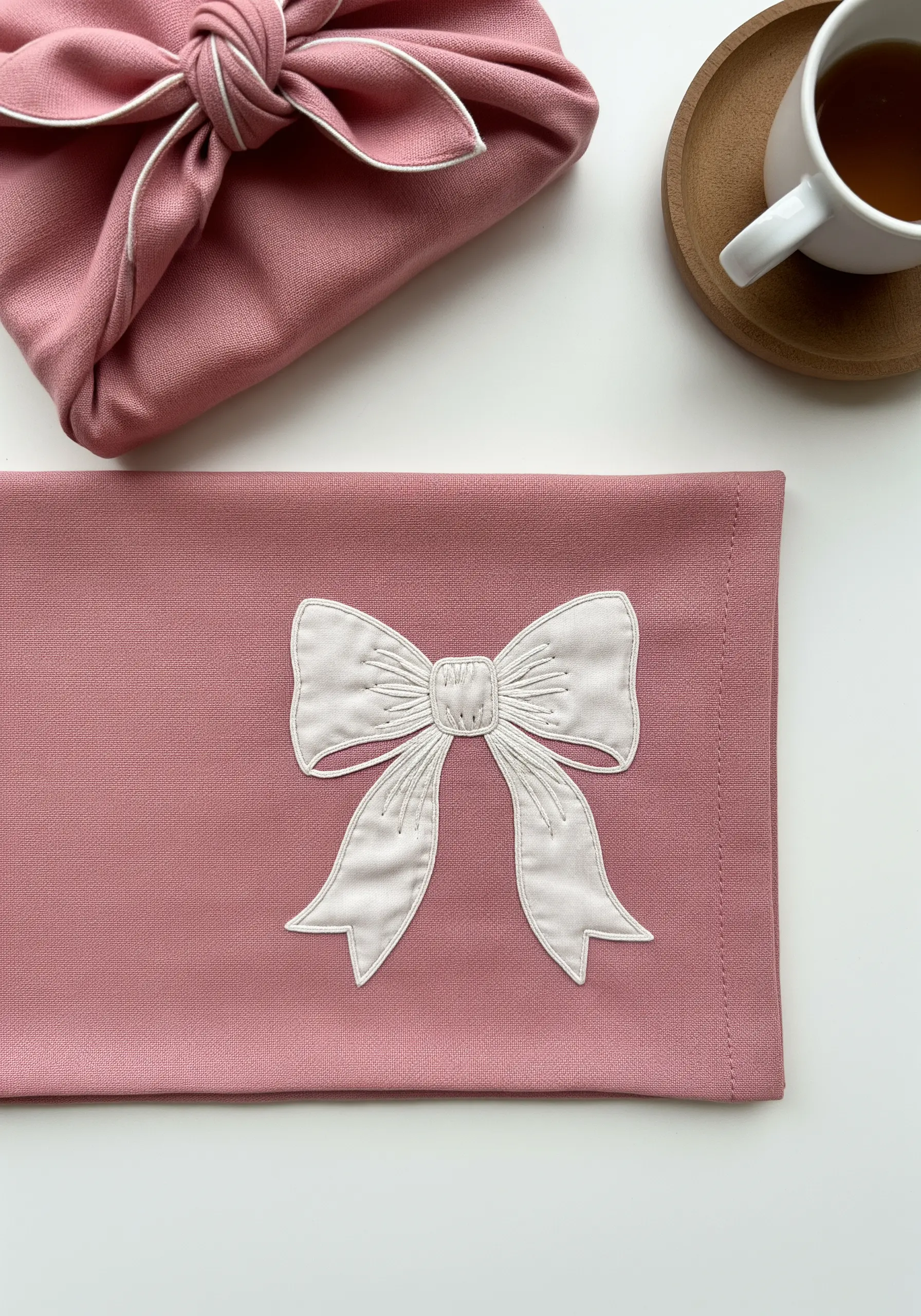 A white fabric appliqué bow detailed with satin stitch edges and line embroidery.
