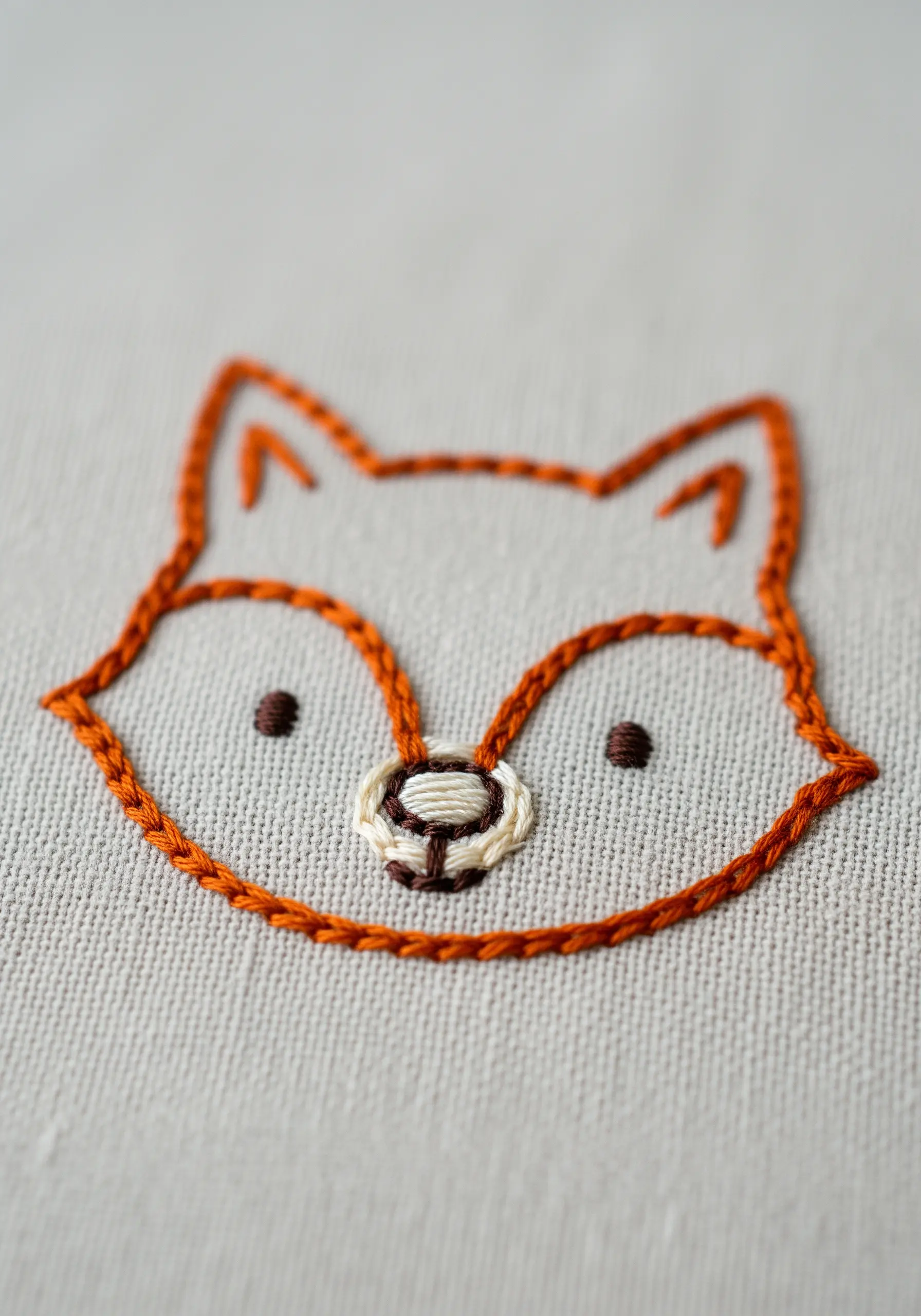A minimal line art embroidery of a fox's face with a chain stitch outline.