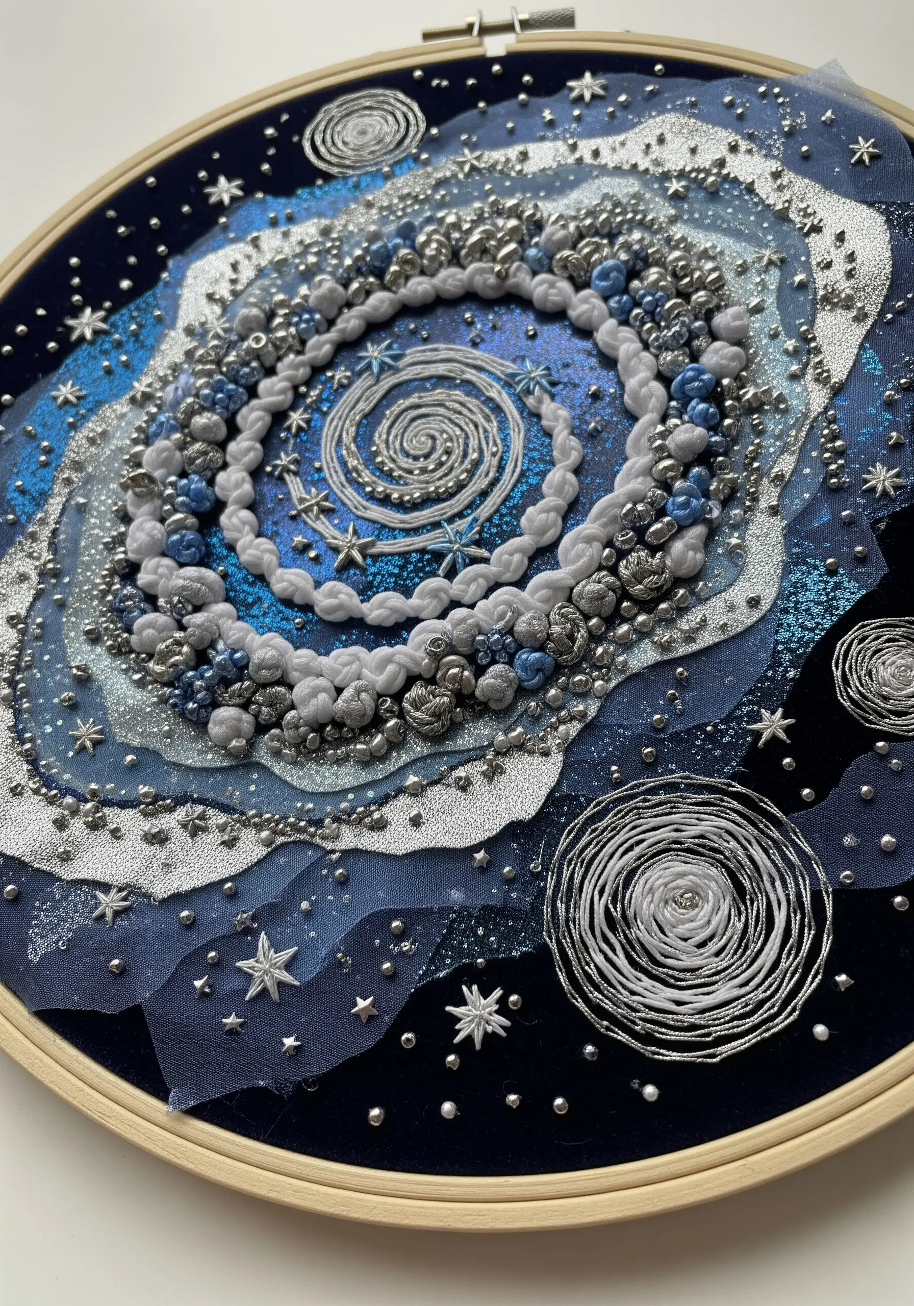 Embroidered galaxy in a hoop with layers of blue tulle, silver beads, and swirling yarn.
