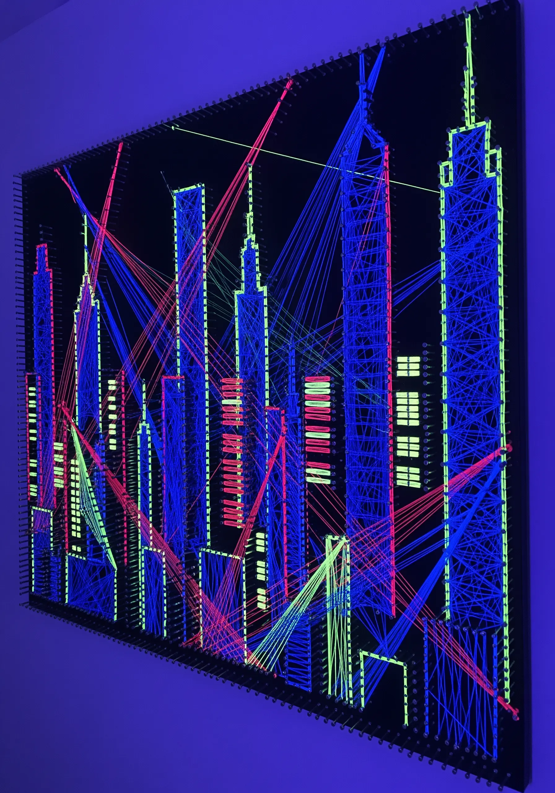 A neon string art cityscape with glowing blue, pink, and lime green threads on a black background.