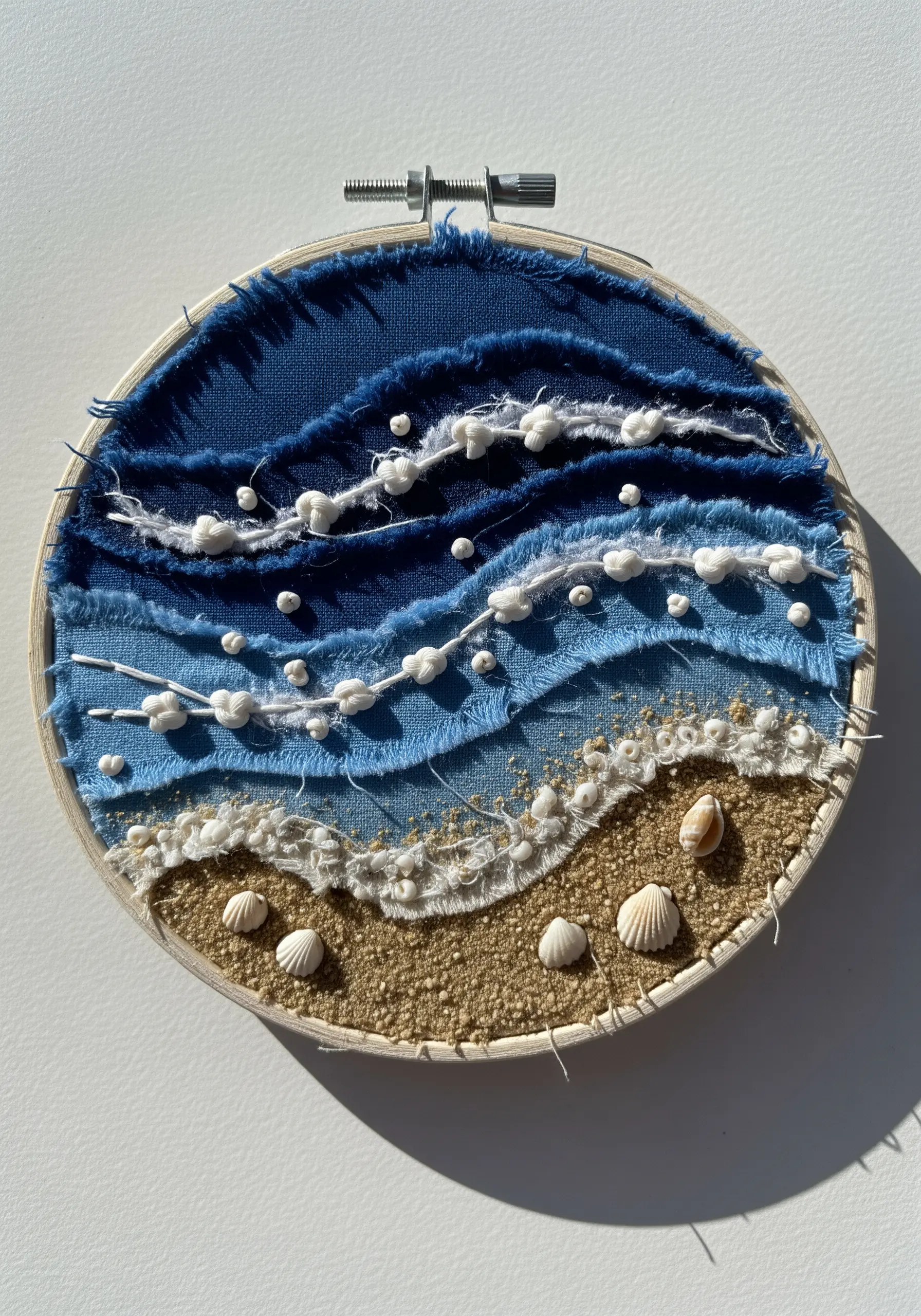 Mixed-media seascape in a hoop using torn fabric, knots, and shells.