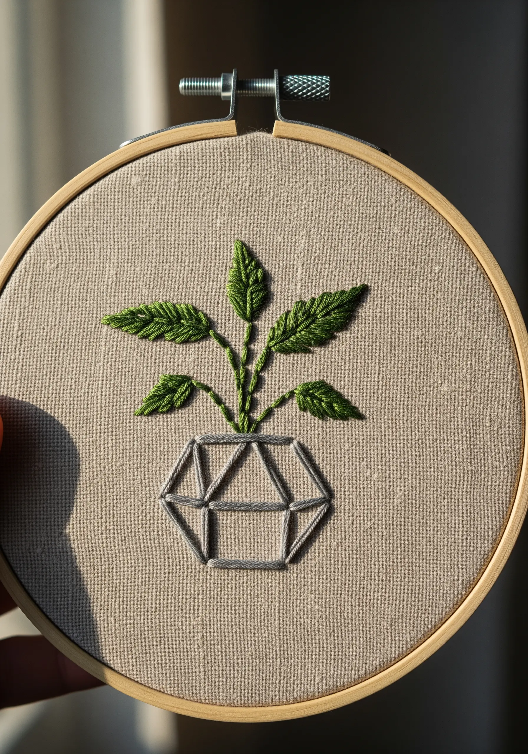 A plant with green fishbone-stitch leaves emerging from a geometric gray-lined pot.