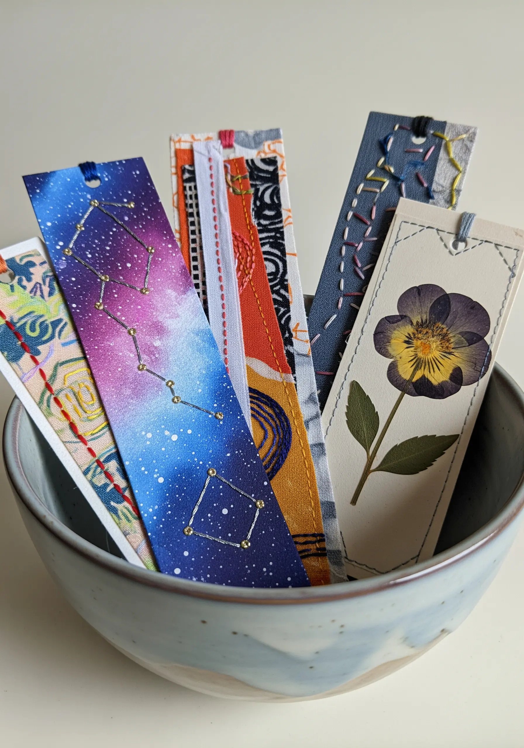 A collection of handmade bookmarks featuring embroidered constellations, fabric scraps, and a pressed pansy.