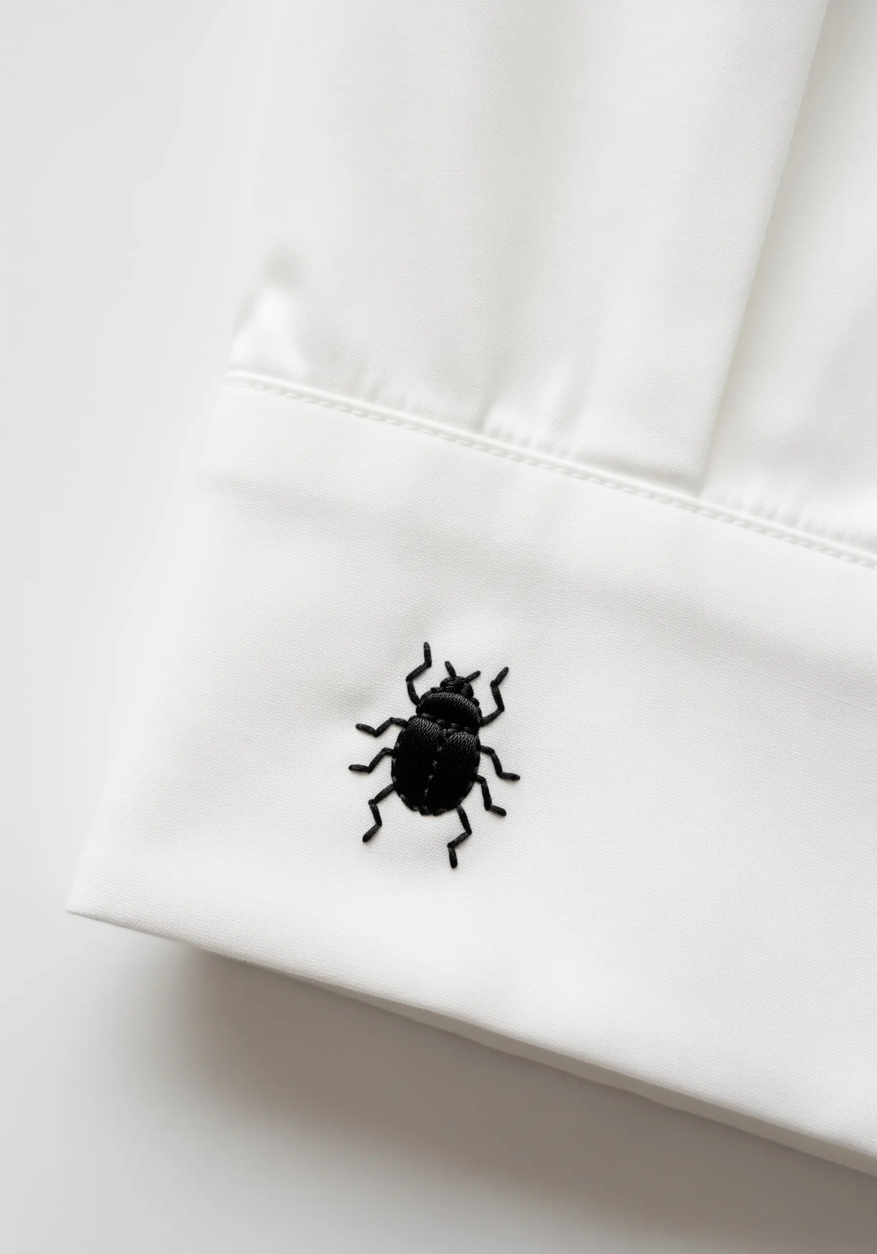 A tiny, solid black beetle embroidered on the cuff of a white dress shirt.