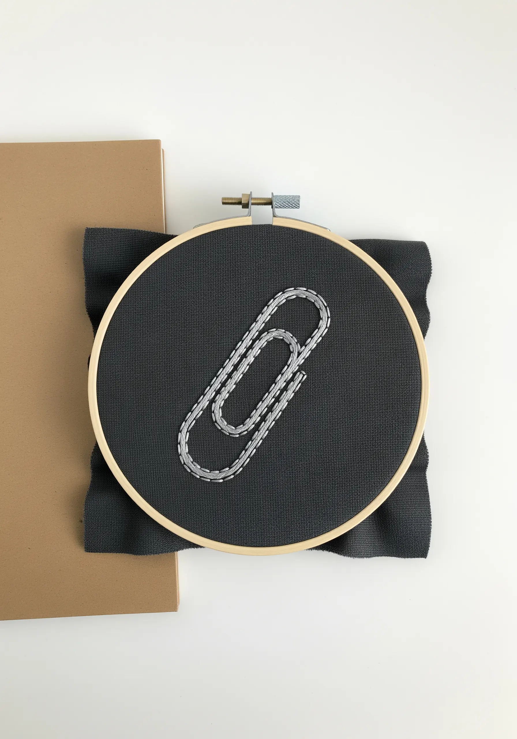 A paperclip embroidered using couching stitch with silver thread on black fabric.