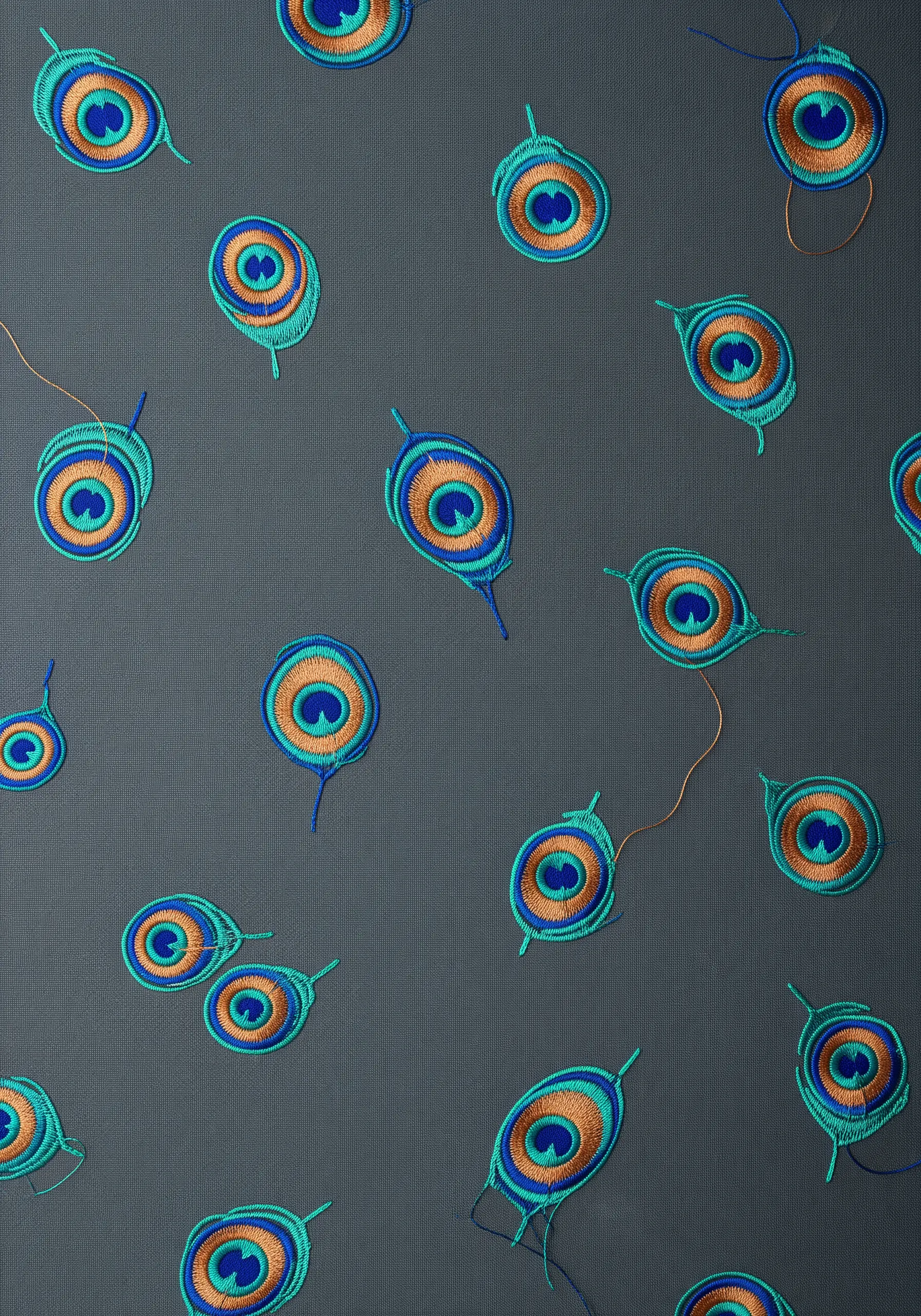A dark gray fabric covered in a random pattern of small, embroidered peacock feather 'eyes'.